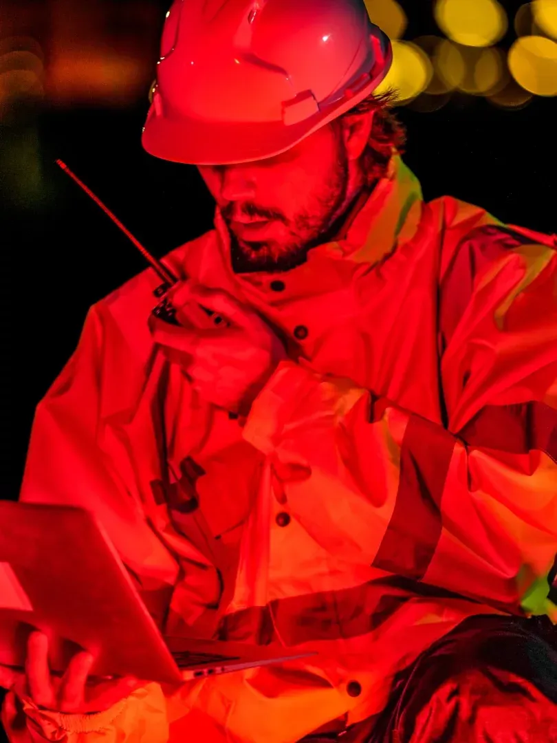 Worker in red hard hat using a walkie-talkie and laptop in red lighting