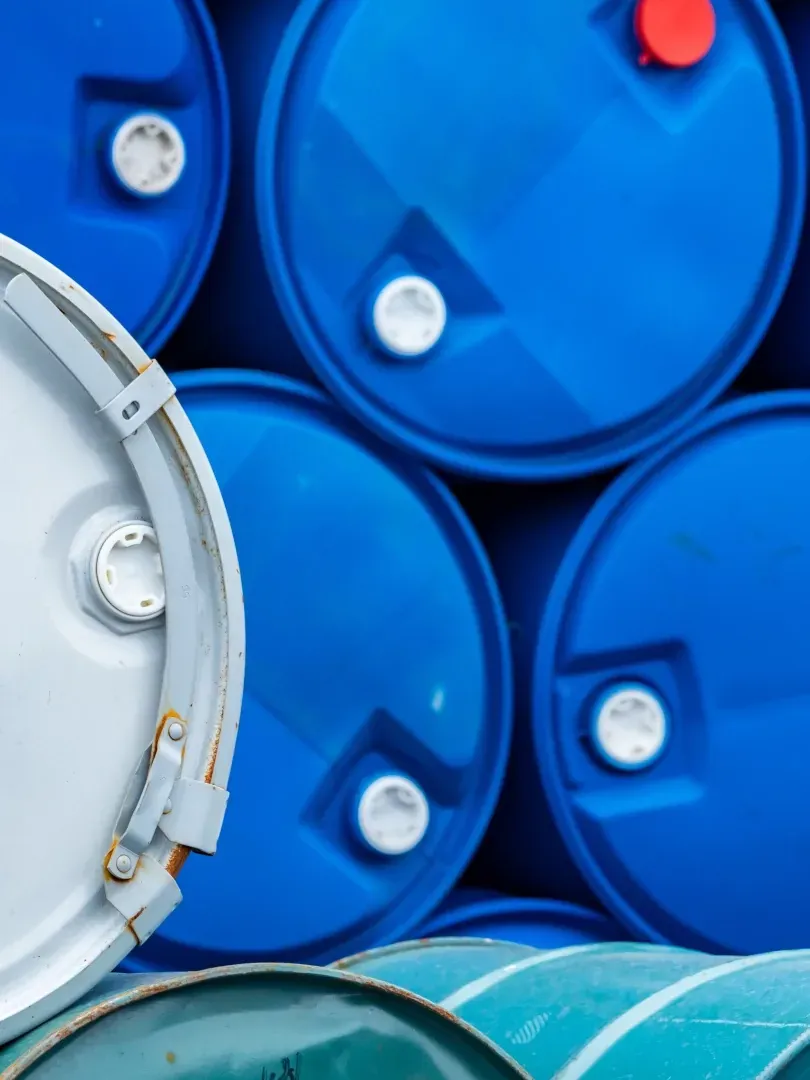 Blue industrial barrels stacked in a storage area, with a white drum edge visible on the left.