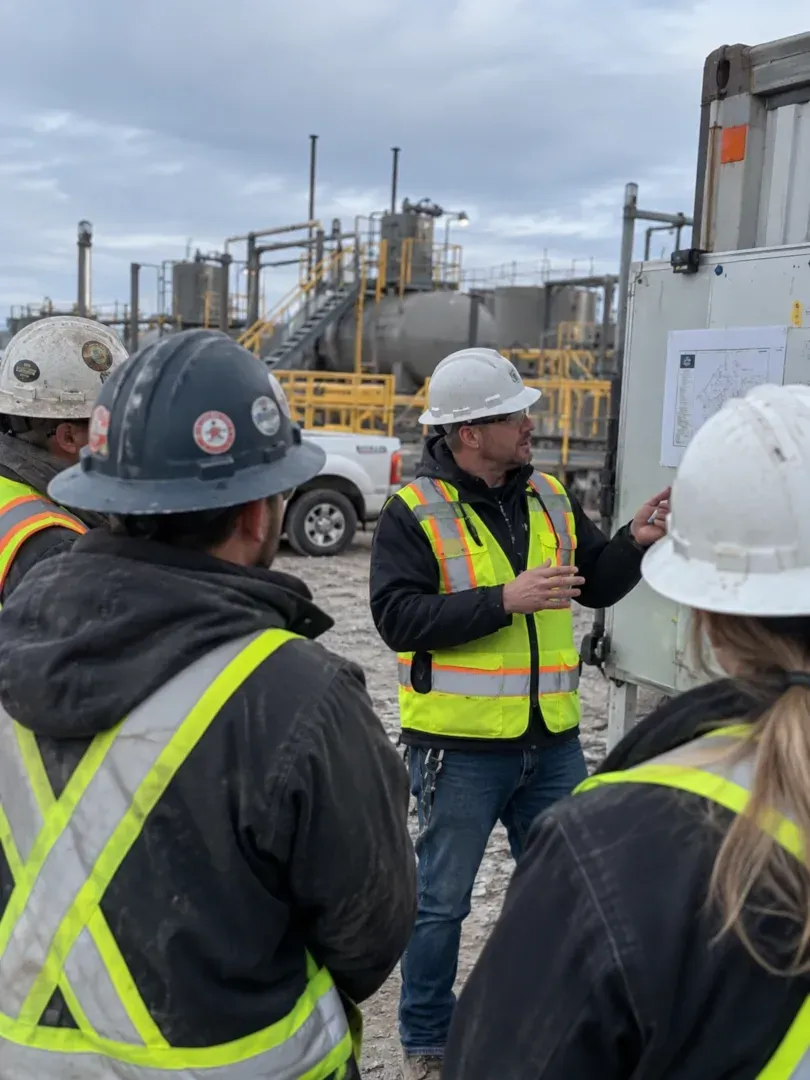 Workers in hard hats and safety vests listening during a site briefing at an industrial facility