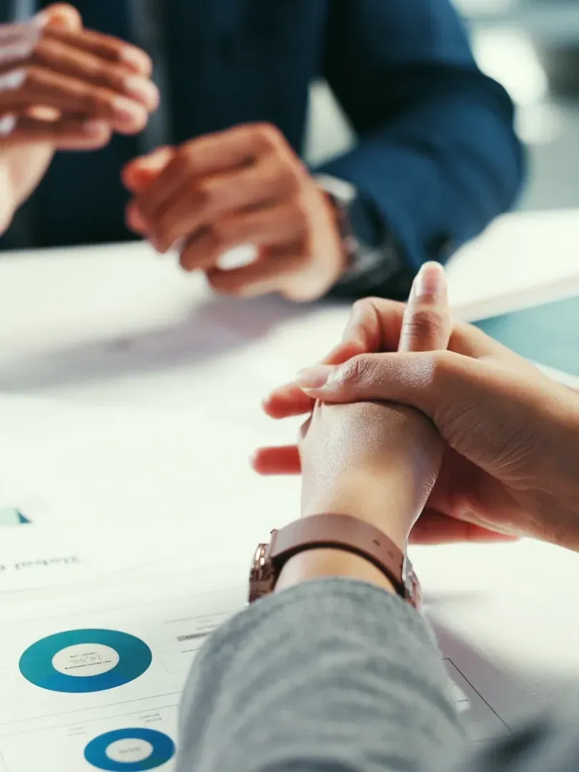 Hands in a business meeting gesturing over a white table with charts and documents