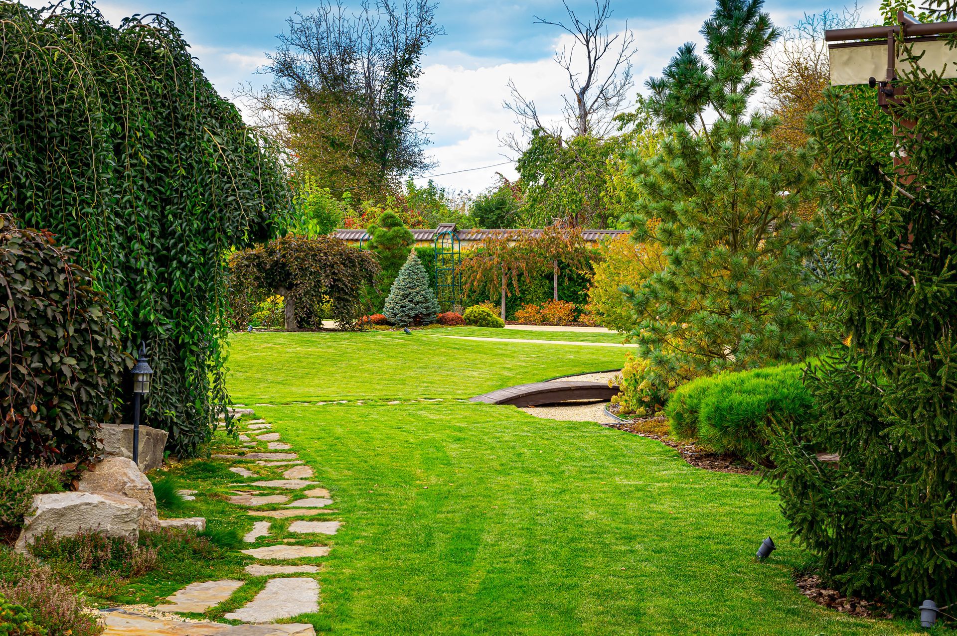 Lush green garden path with stone edging, shrubs, and trees leading to a landscaped lawn.