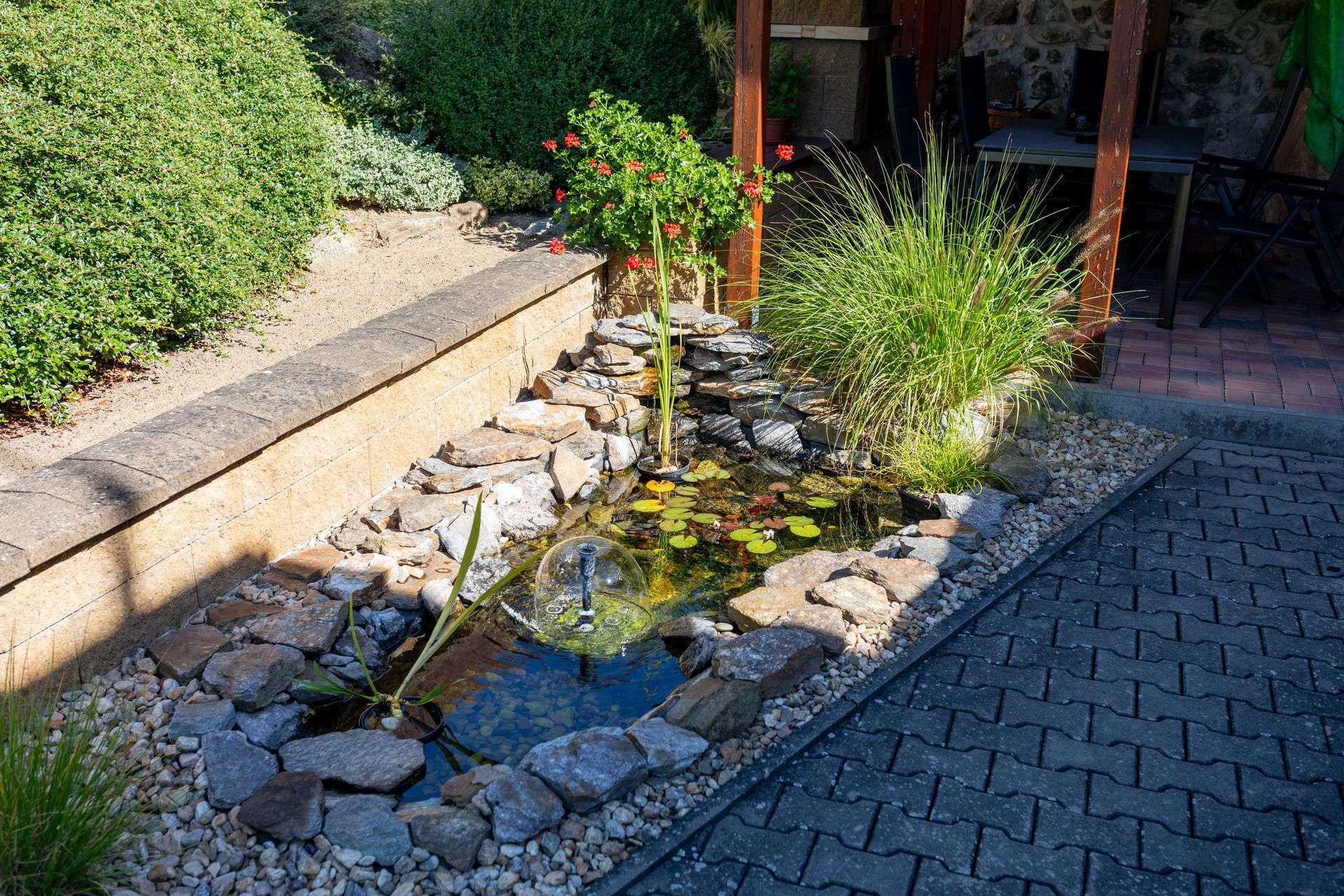 Small garden stream with rocks, plants, and a paved patio beside it
