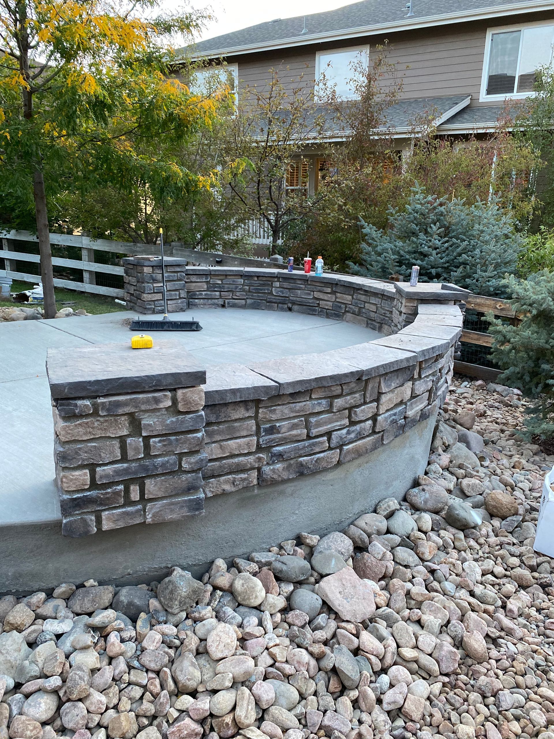 A brick wall is surrounded by rocks in a backyard in front of a house.