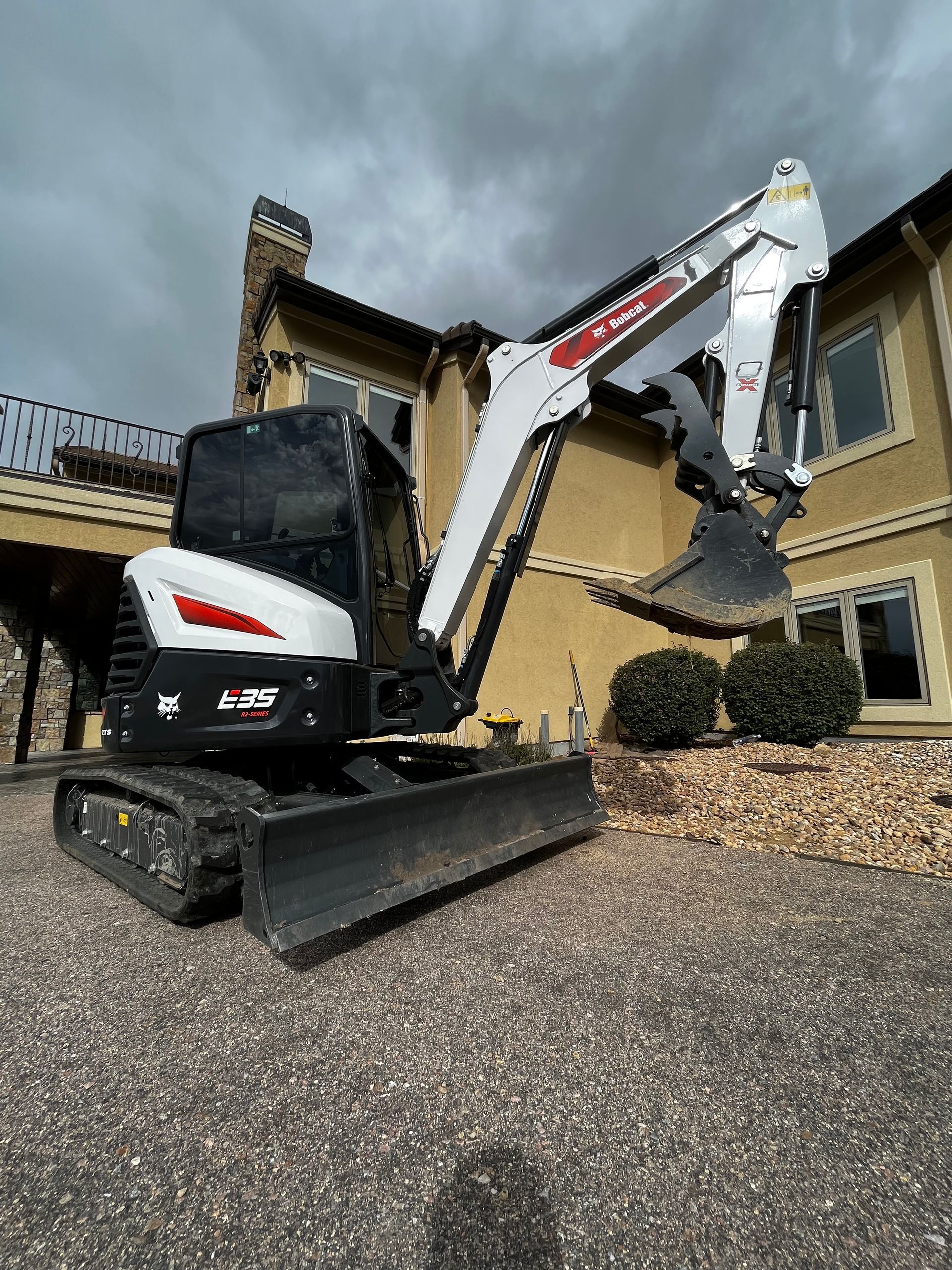 A small excavator is parked in front of a large house.
