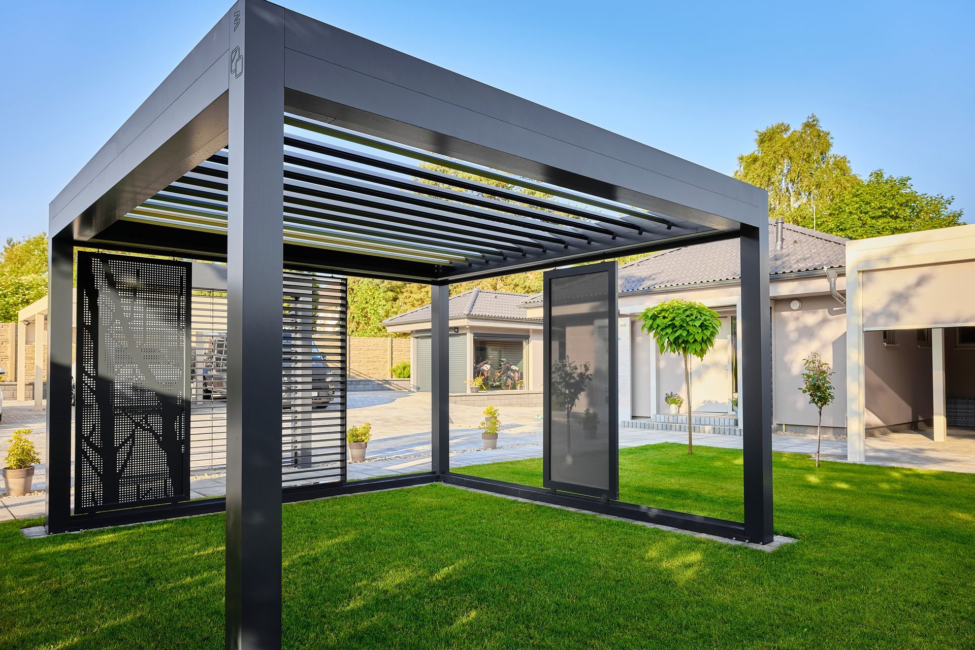 A black pergola is sitting on top of a lush green lawn in front of a house.