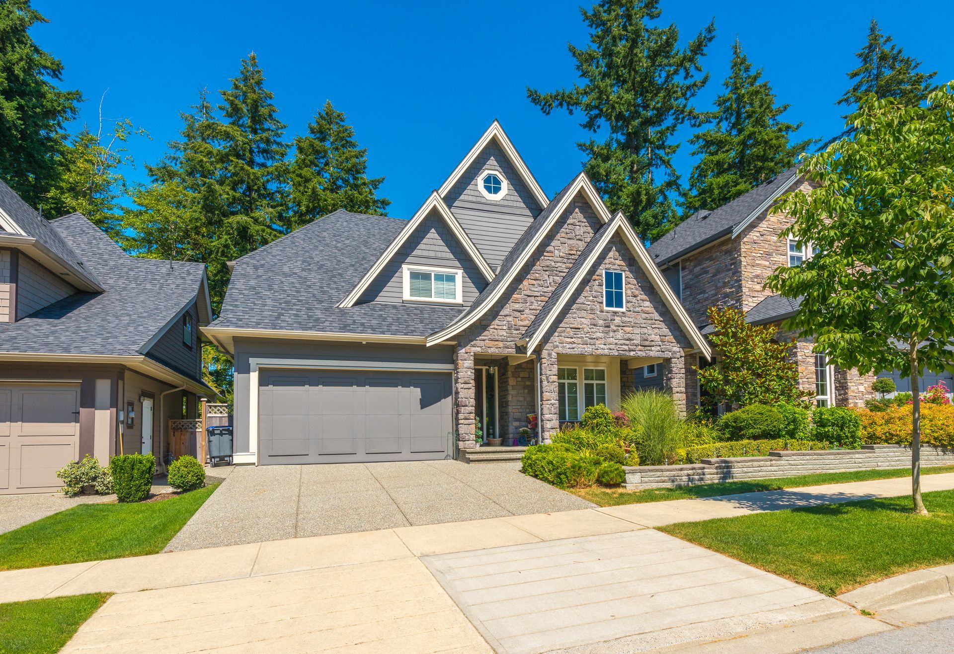 A large brick house with a gray garage door is sitting on a lush green residential street.