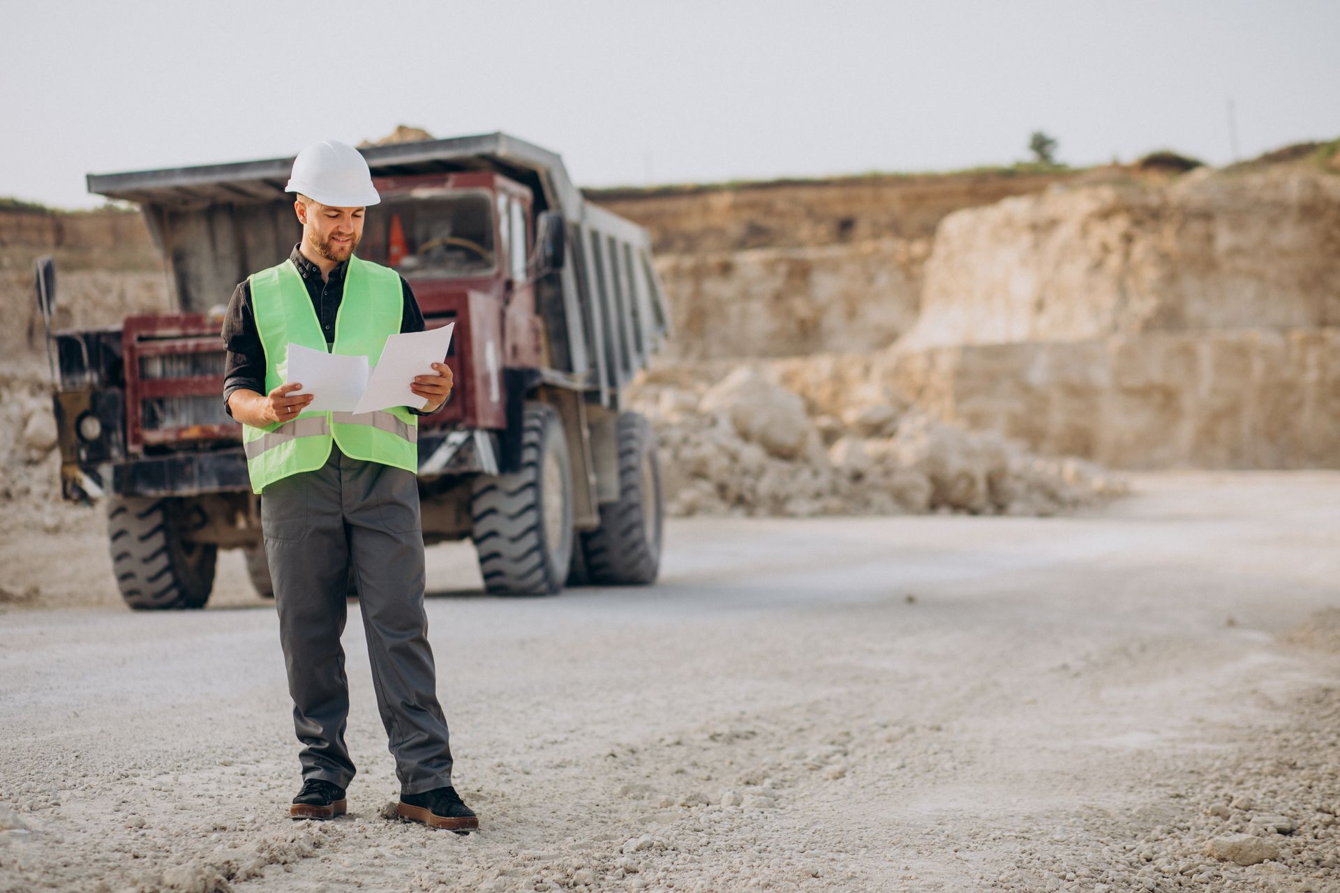 A man is standing in front of a dump truck in a quarry.