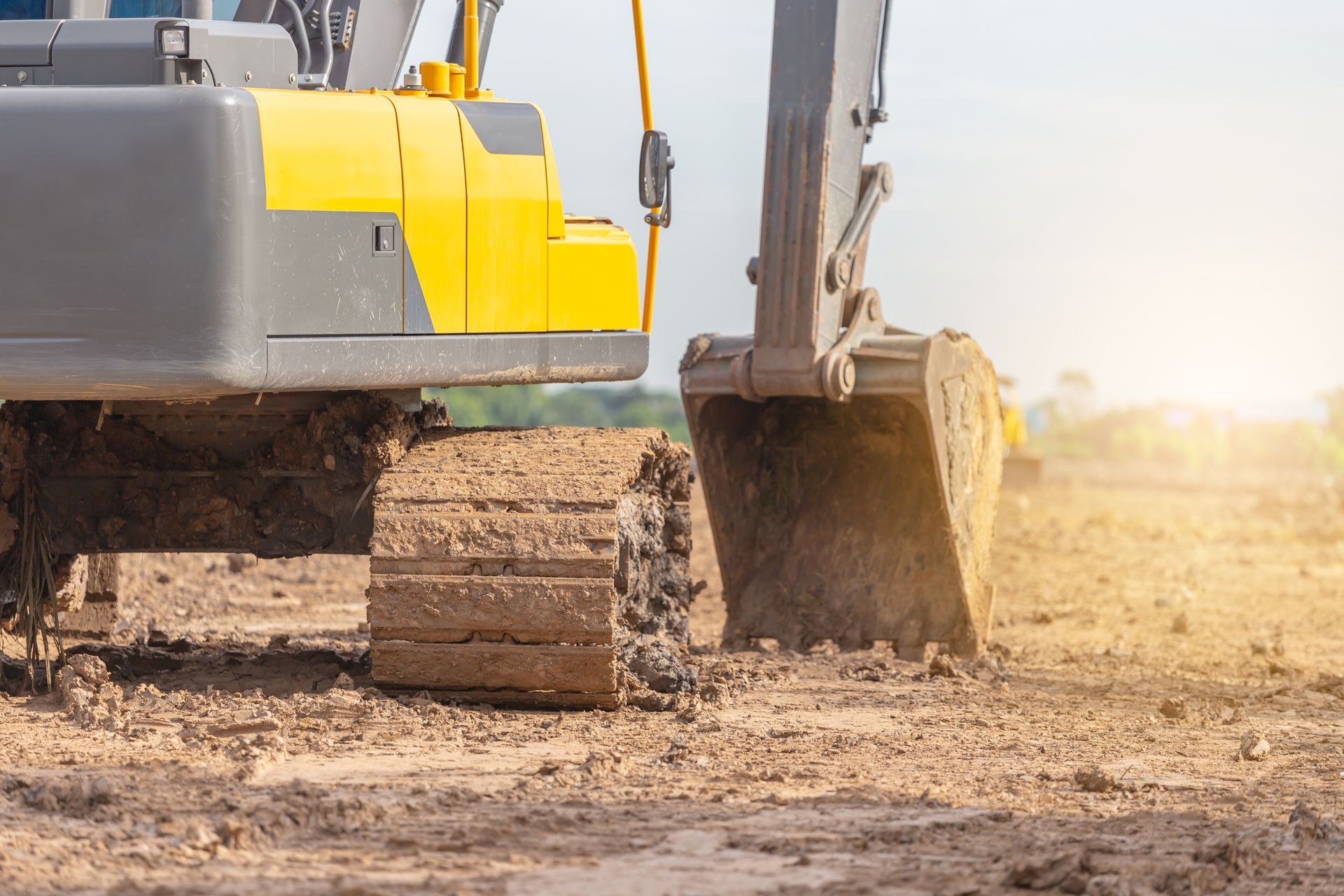 A yellow and gray excavator is digging a hole in a dirt field.