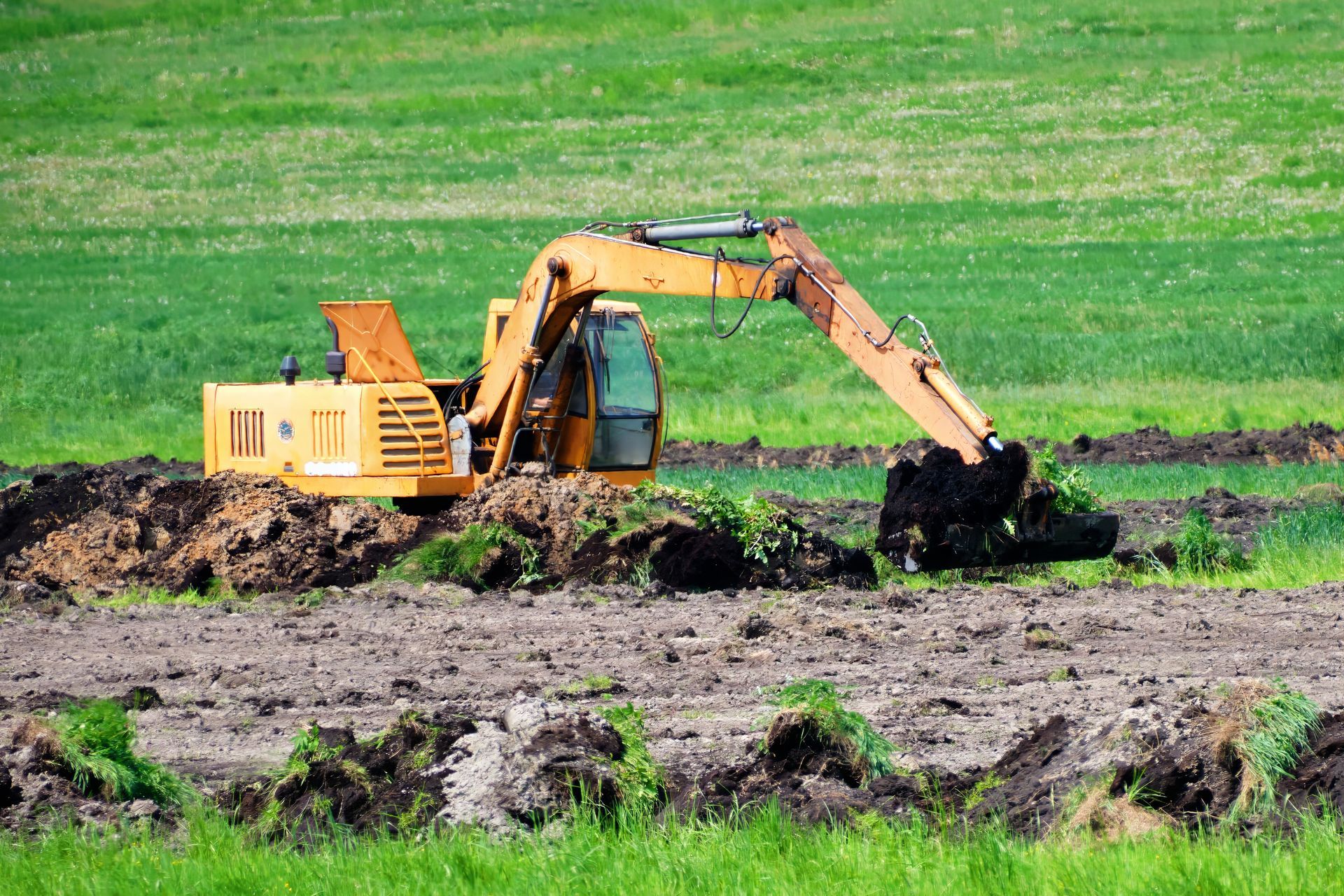 A yellow excavator is digging a hole in a field.