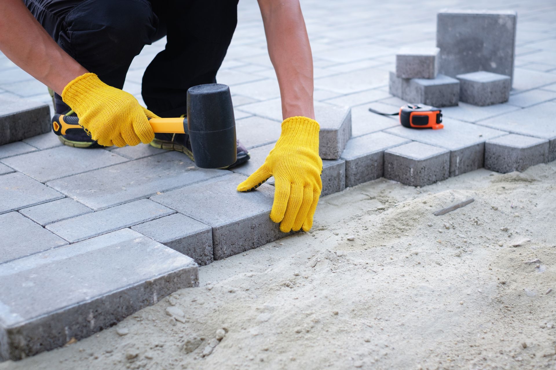 A man is laying bricks on a sidewalk with a hammer.