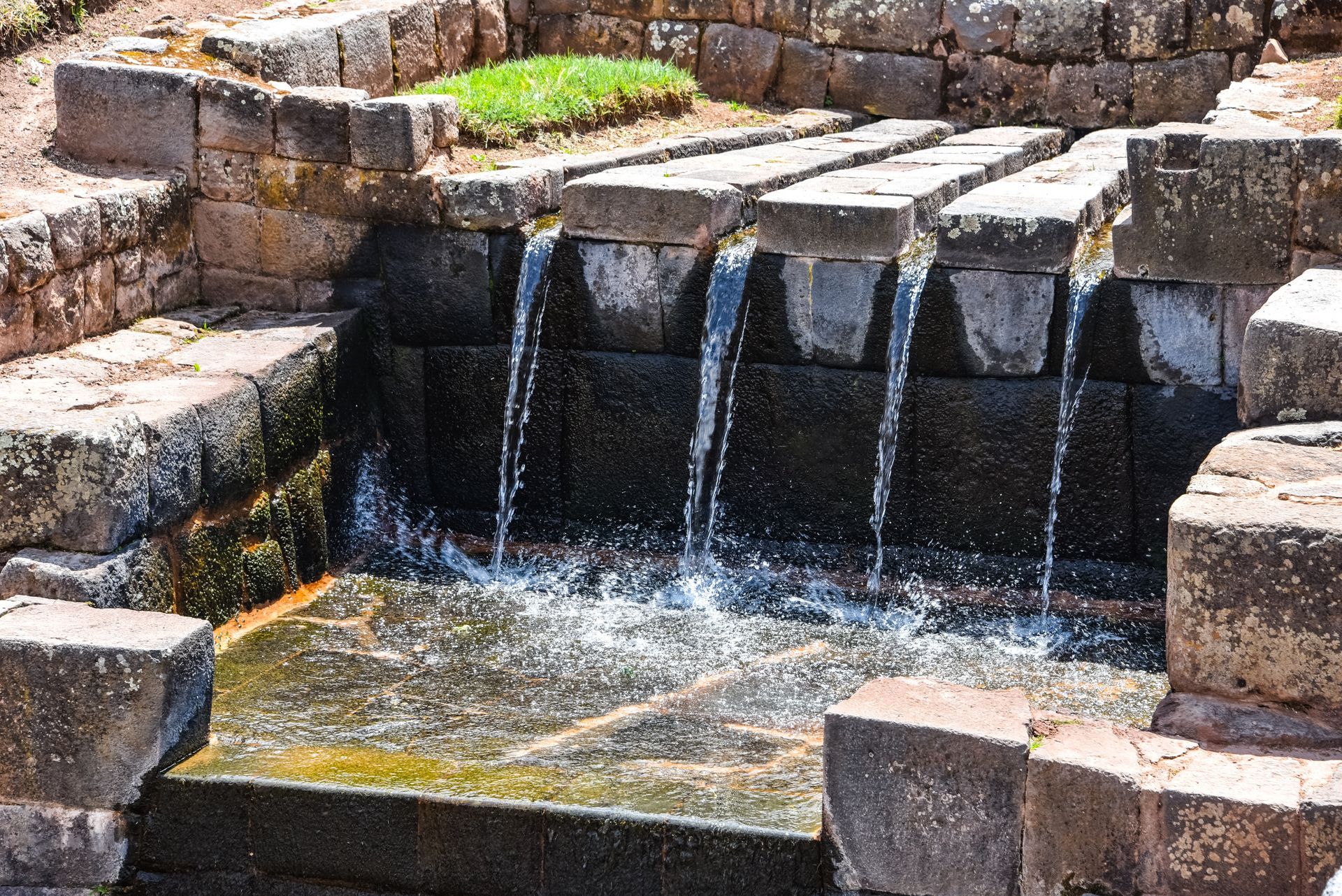 A waterfall is surrounded by a stone wall and steps.