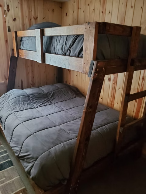 Wooden bunk bed with gray bedding in a small wood-paneled room
