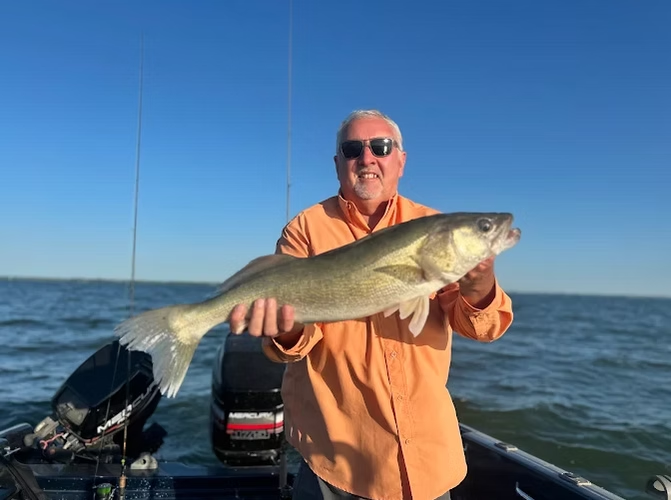 Man in orange shirt holding a large fish on a boat with open water and blue sky behind him