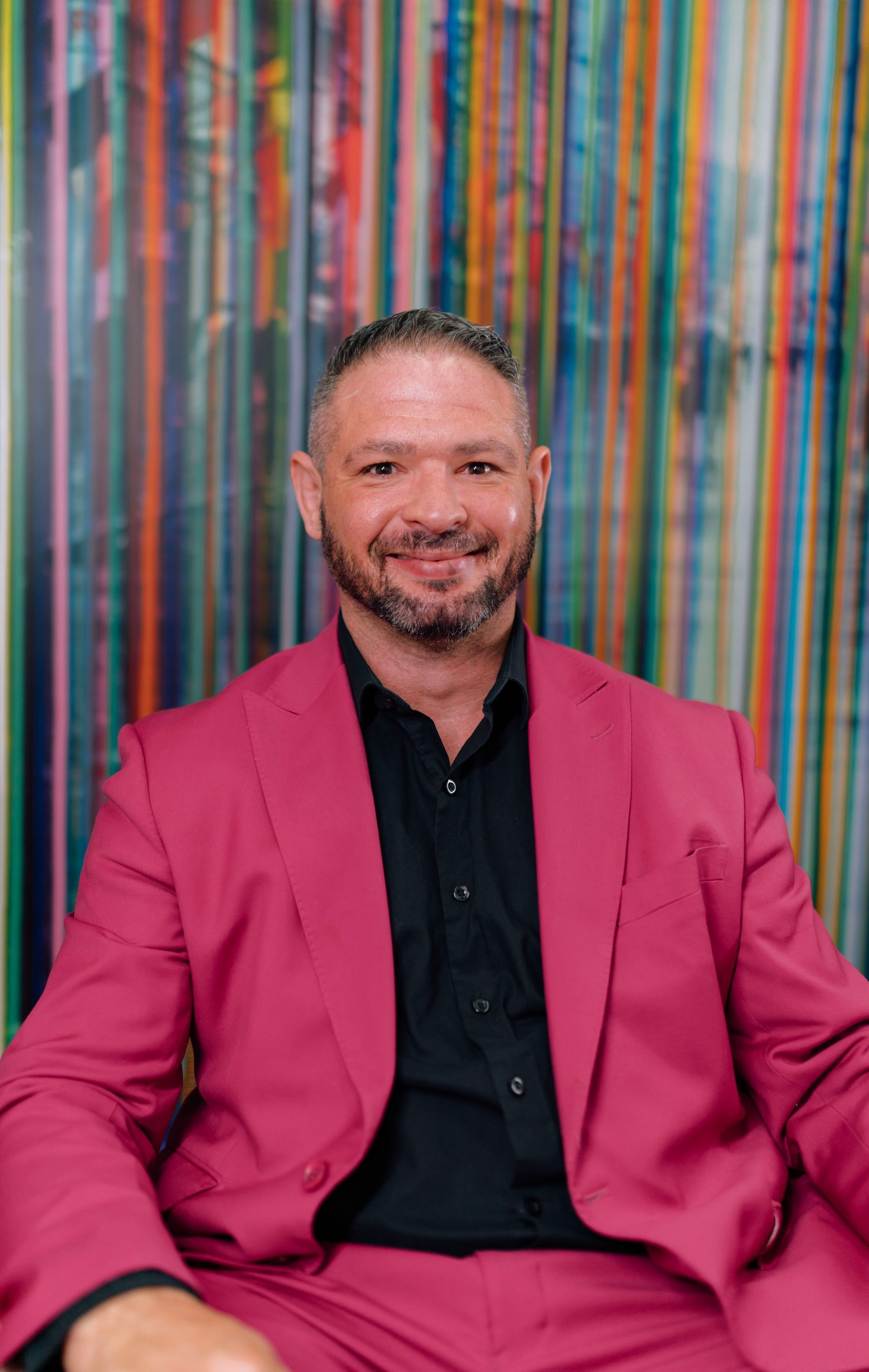 a man in a pink jacket and black shirt is standing in front of a bookshelf .