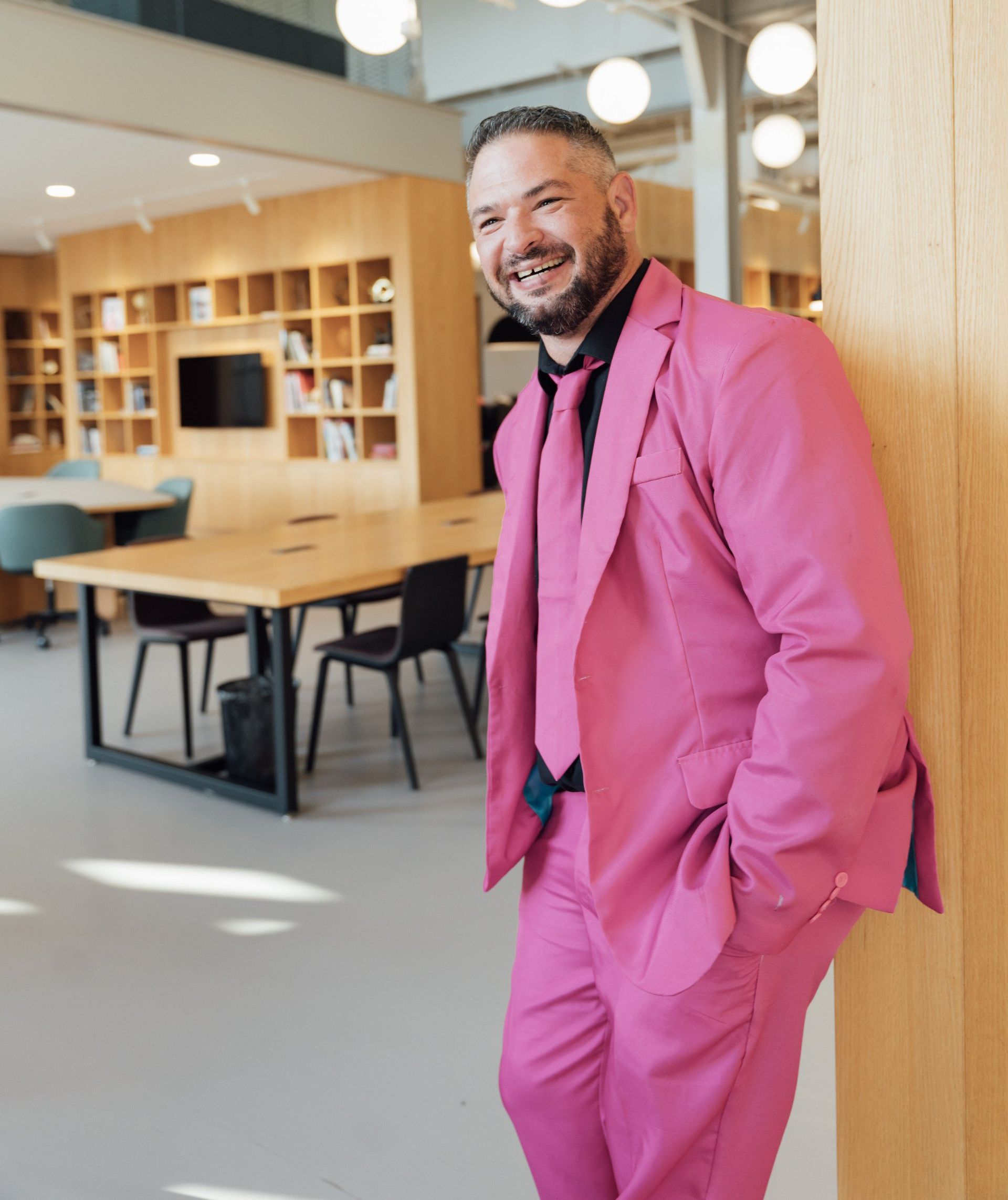 a man in a pink suit and tie is leaning against a wall .