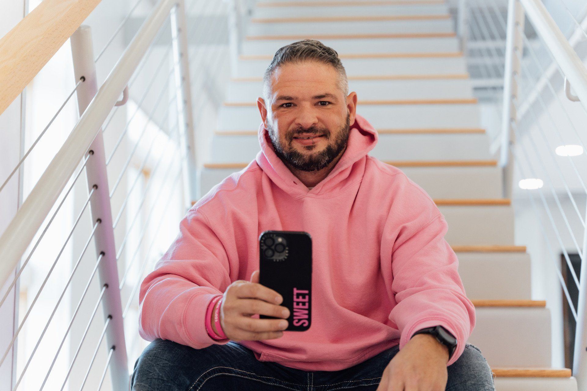 a man in a pink hoodie is sitting on a set of stairs holding a cell phone .