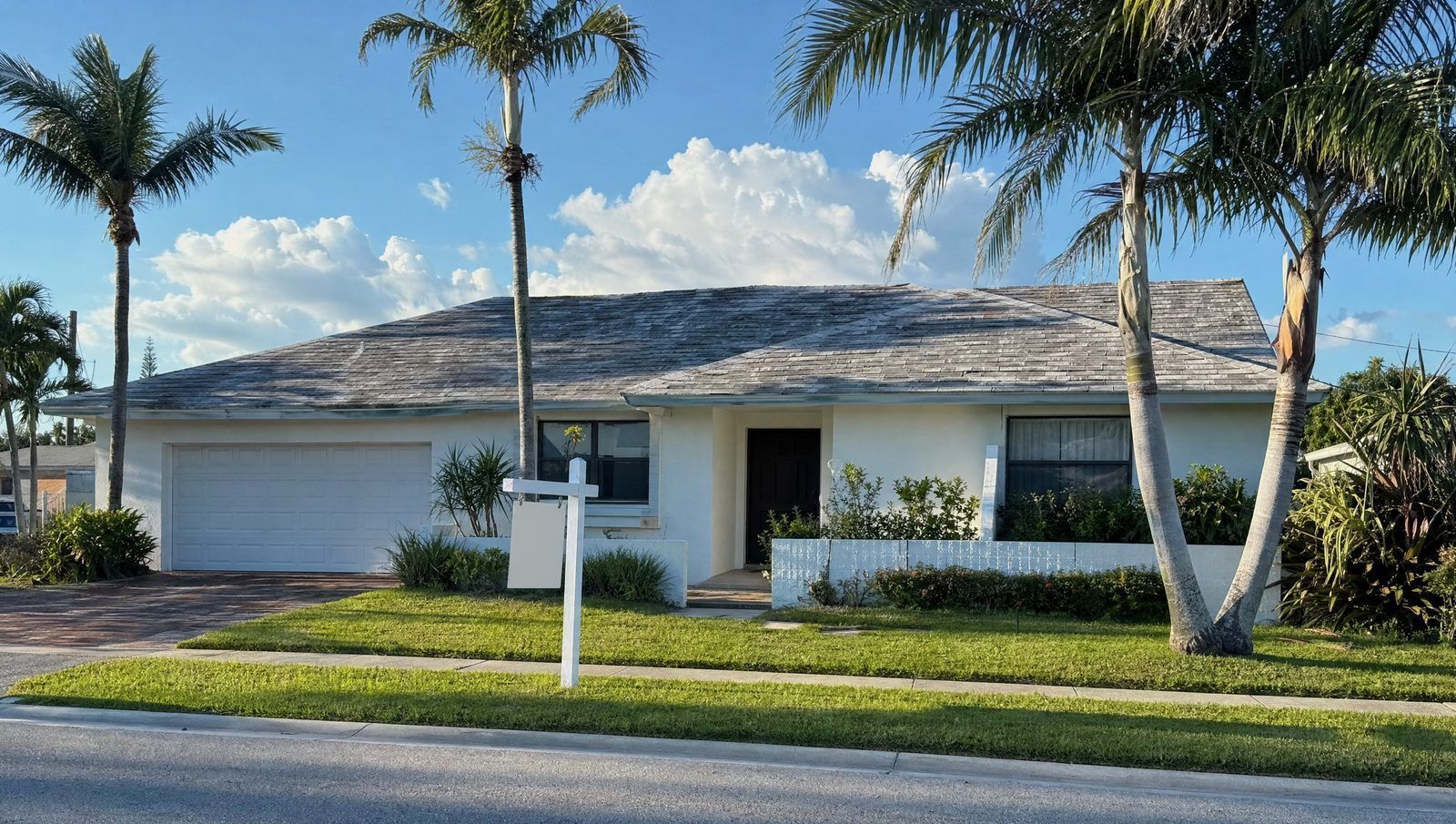 Single-story South Florida home with a sun-faded, aging shingle roof and a for-sale sign in the fron