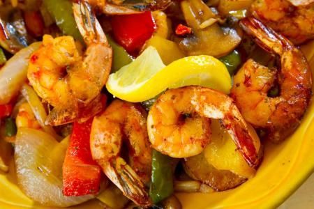 A close-up of a shrimp stir-fry with colorful bell peppers, onions, and mushrooms, garnished with a wedge of lemon.