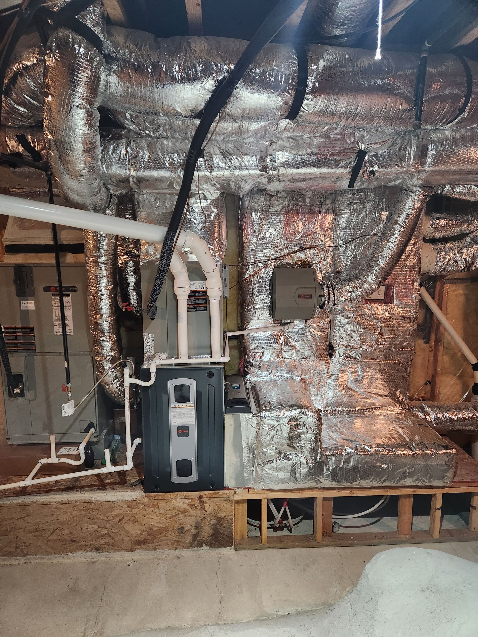 HVAC system in a basement. Ductwork and a water heater are visible, with metallic insulation.