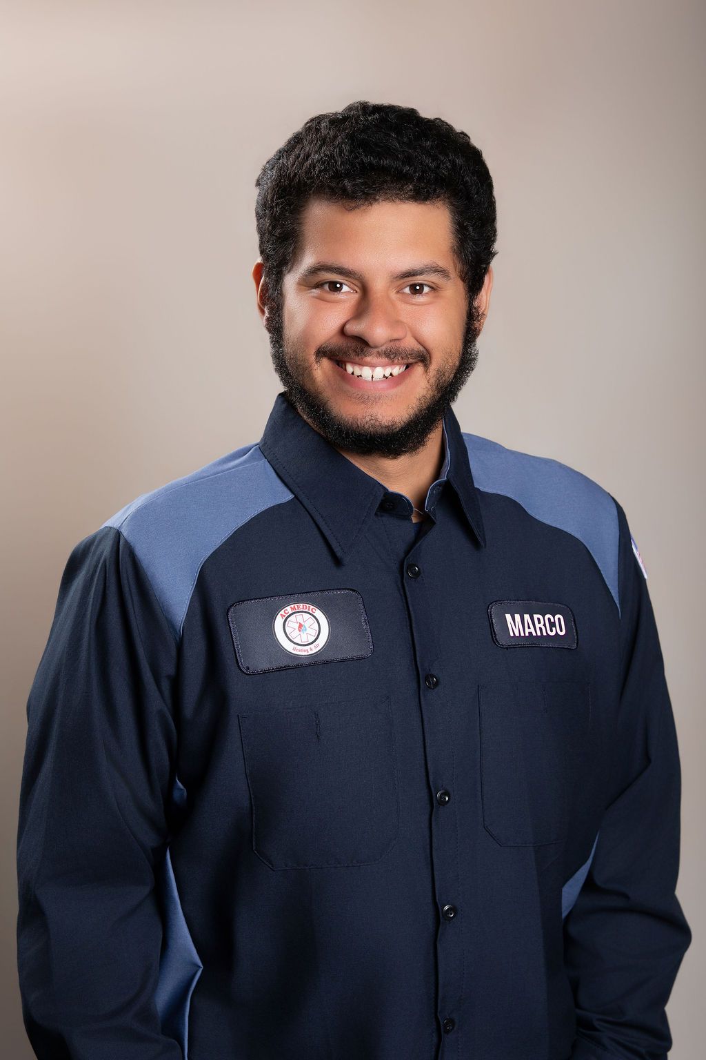 Man in navy work uniform smiling against a plain studio background