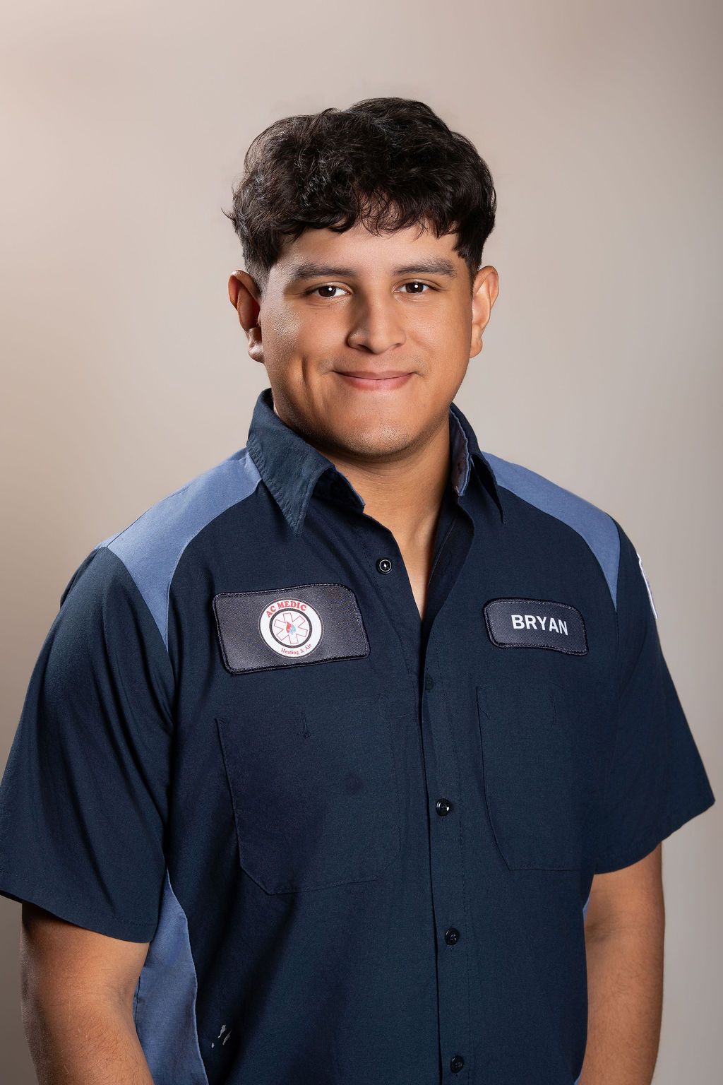 Person in a navy work shirt with embroidered patches, standing against a plain beige background.
