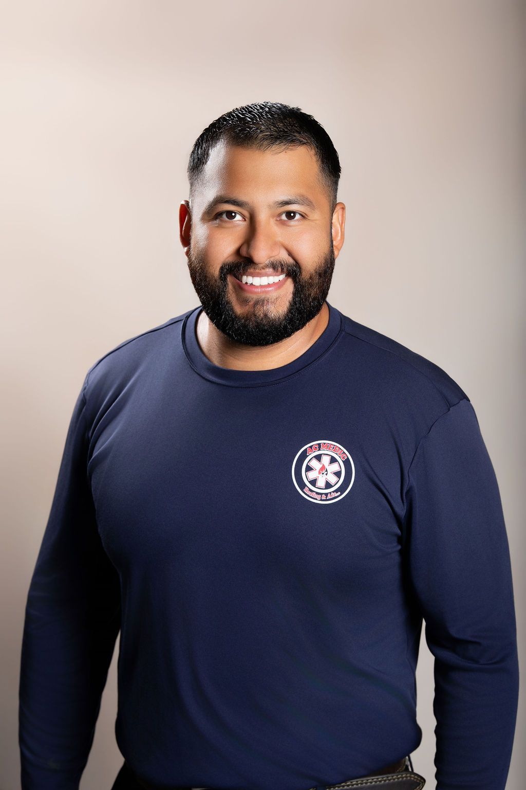 Smiling person in a navy long-sleeve shirt with a small circular logo on the chest, against a light studio background