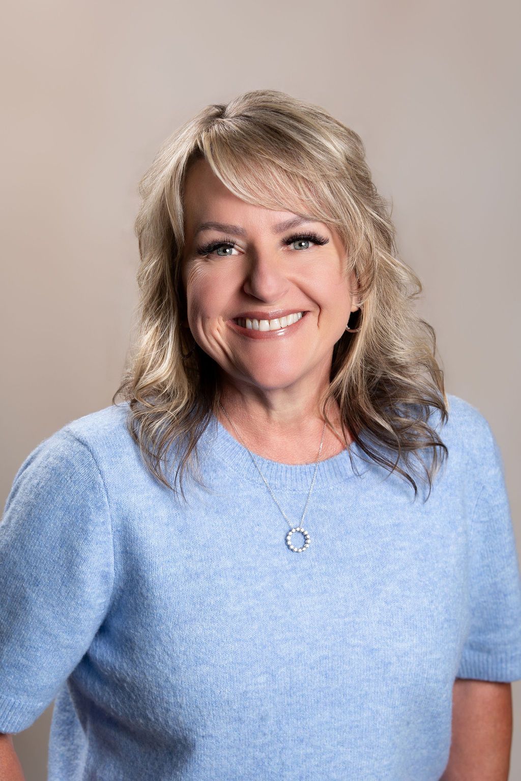 Smiling woman with blonde hair wearing a light blue sweater against a neutral background