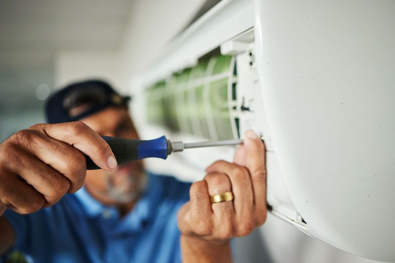 Person using a screwdriver to repair a white air conditioning unit.