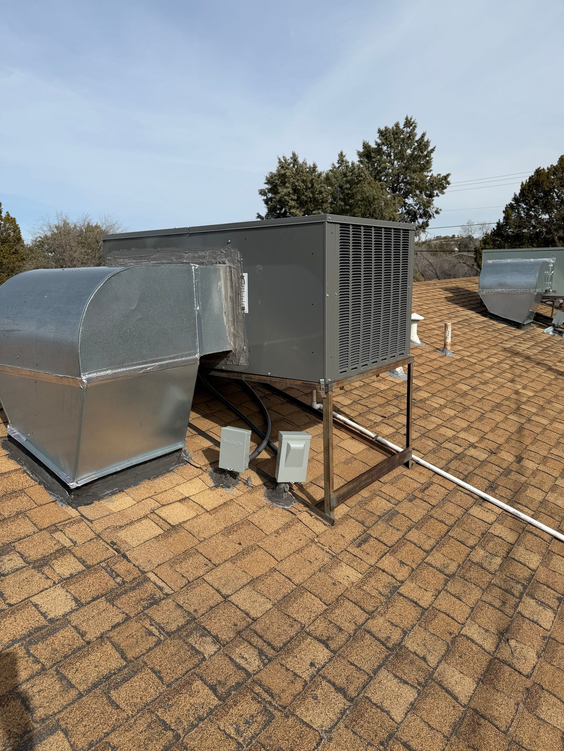 Rooftop HVAC unit with metal vent and ducting on a shingled roof under a clear sky