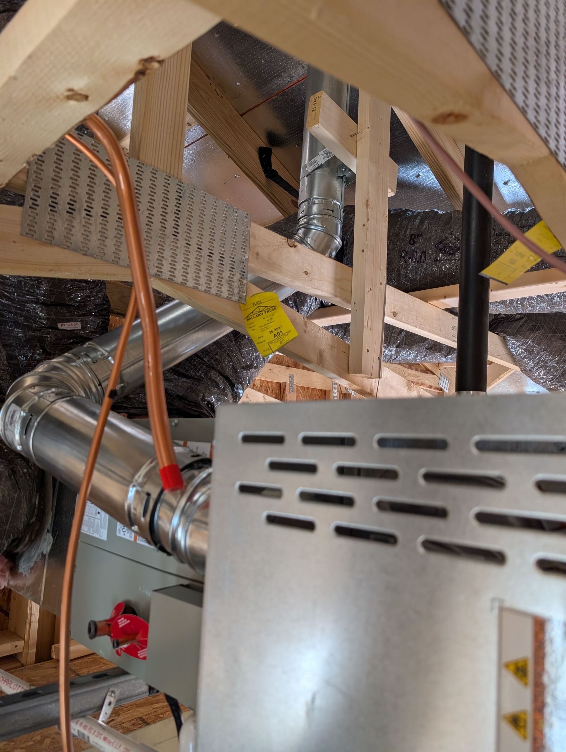 Furnace installed in an attic with copper tubing, ductwork, and wooden supports.