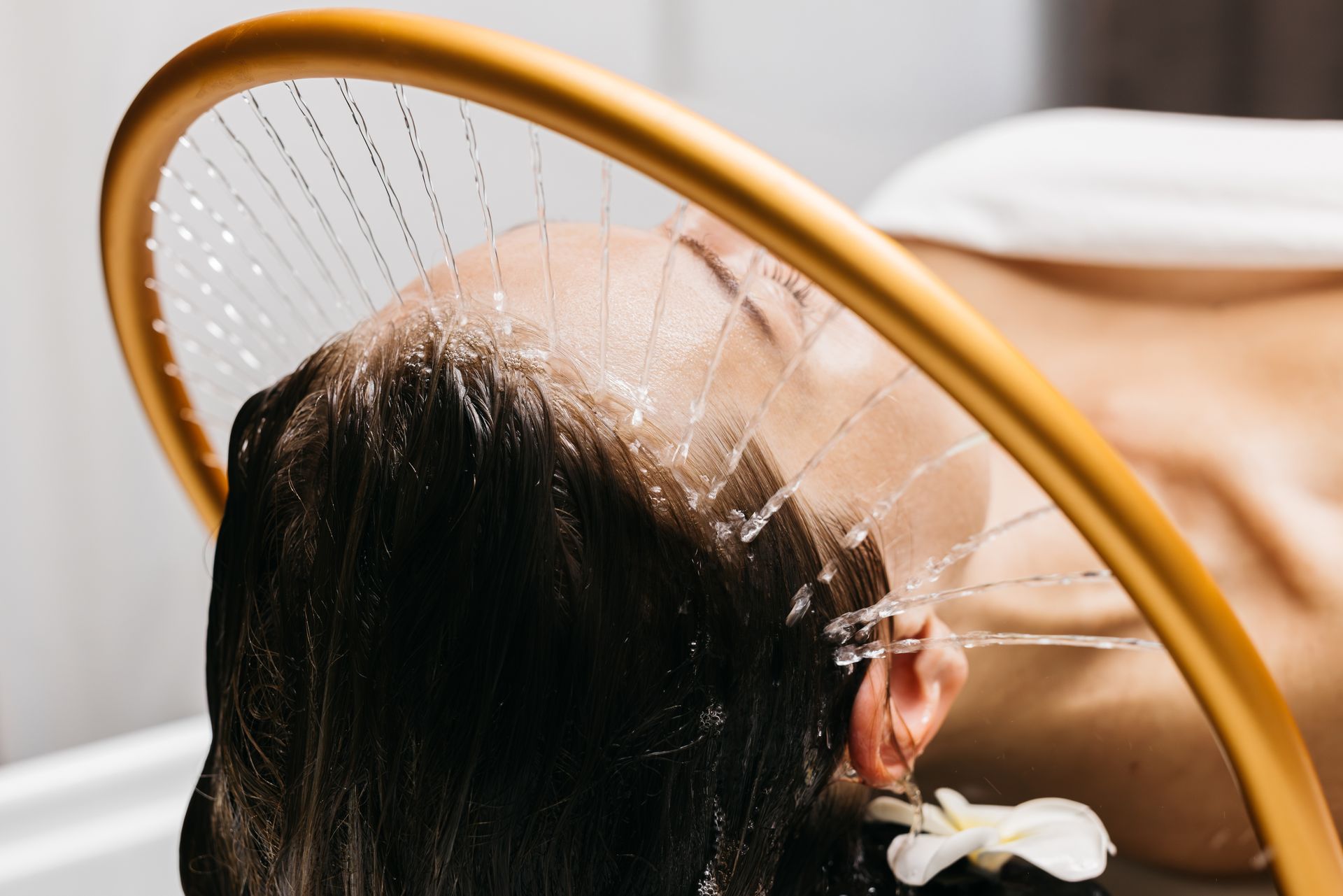 Person rinsing hair under a showerhead through a yellow hoop in a sink