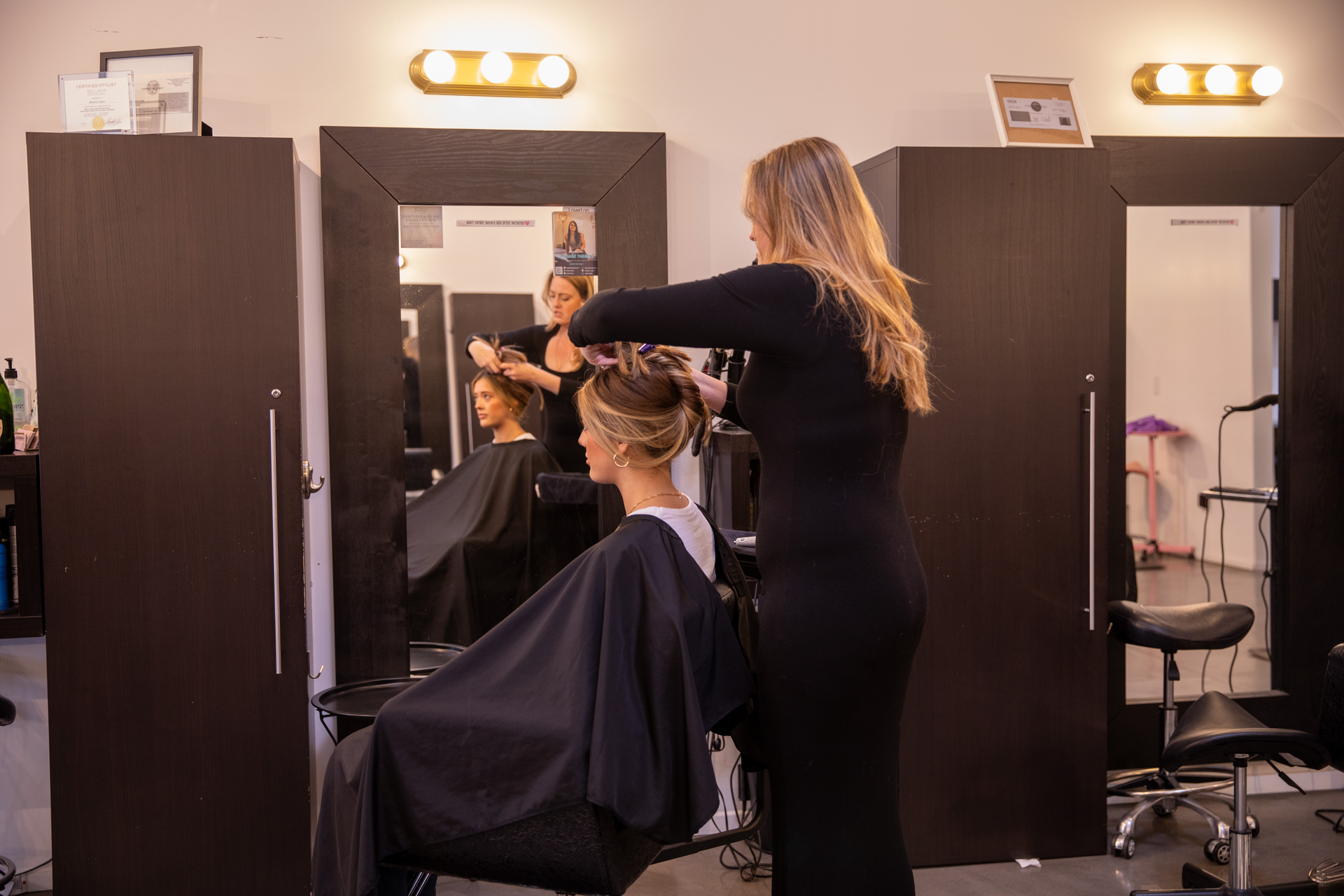 Stylist cutting a client’s hair in a salon with mirrors and dark styling stations