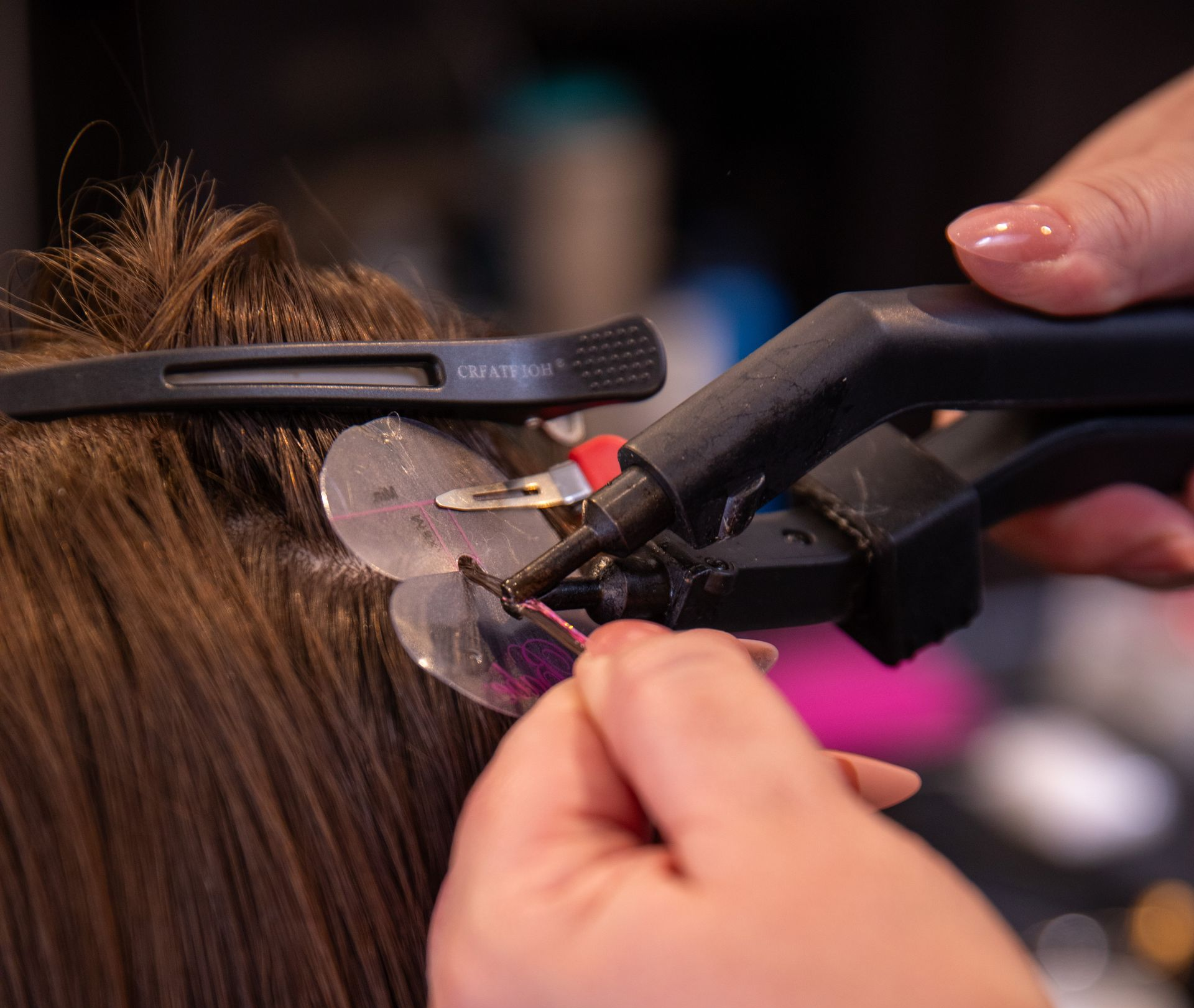Hairdresser using a curling iron on brown hair, with clips holding sections in place.