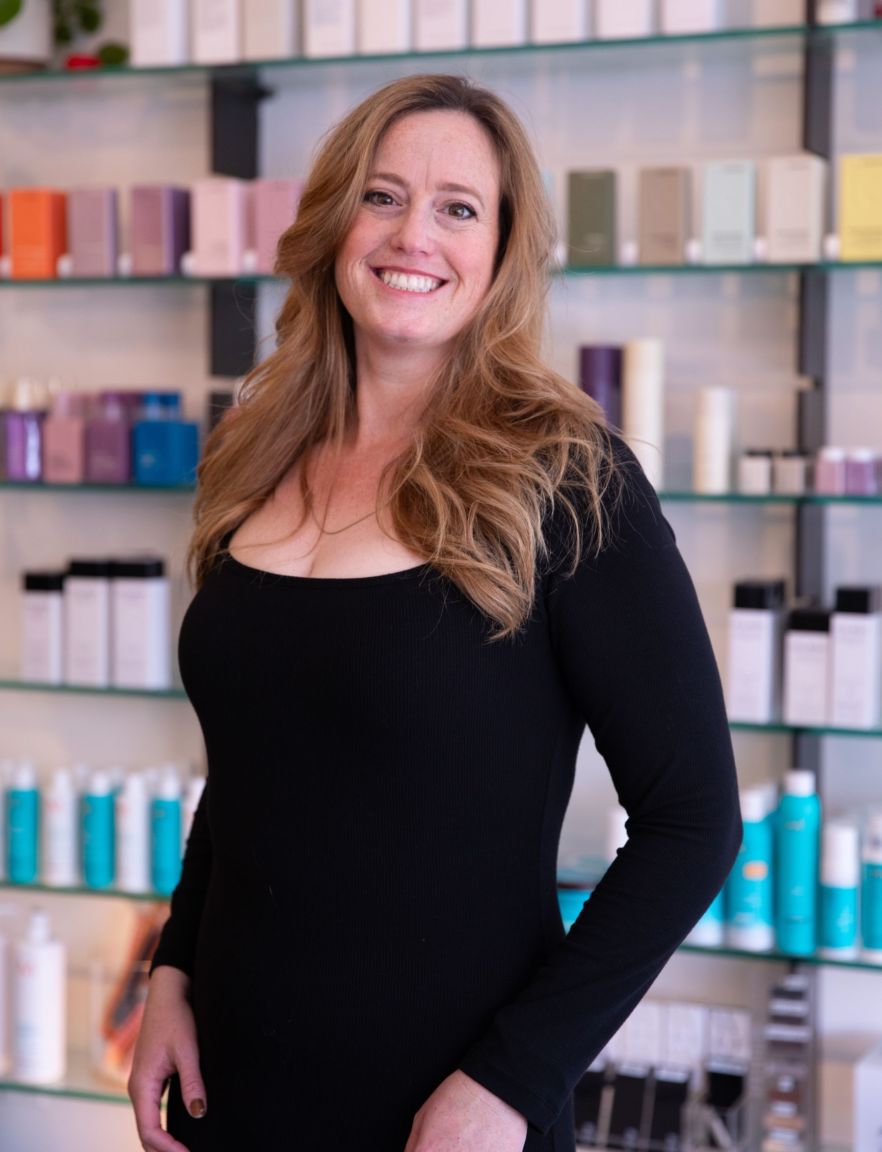 Smiling woman in a black dress standing in front of shelves of colorful product bottles