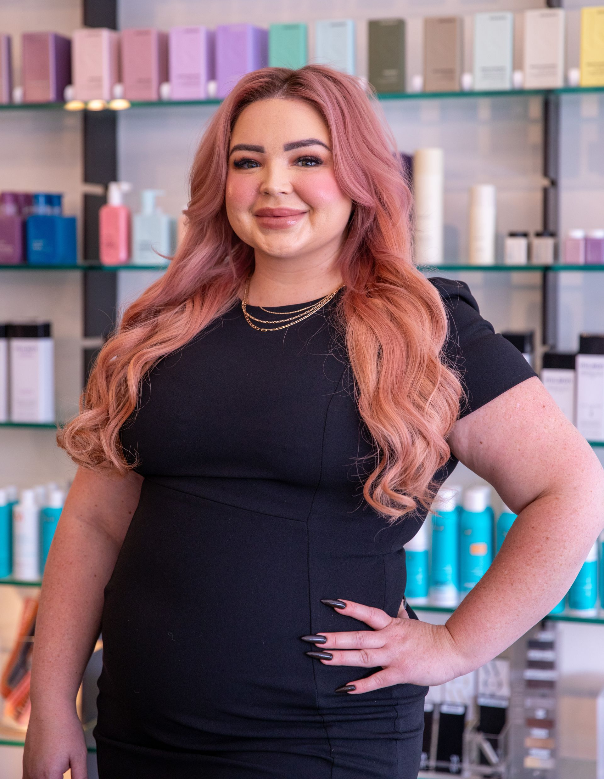 Woman in a black dress standing confidently in front of colorful product shelves.