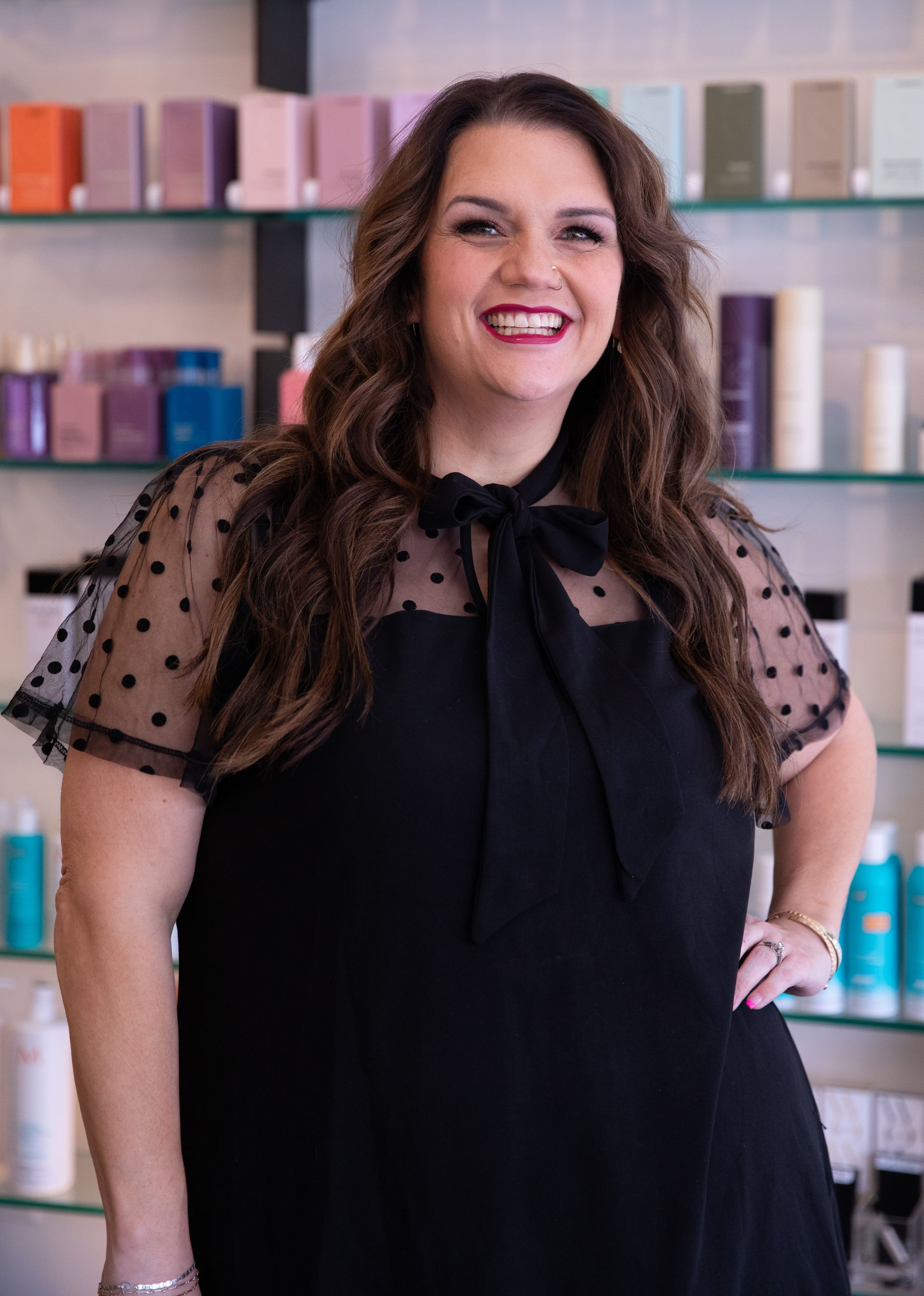 Smiling woman in a black dress standing in front of shelves of colorful products