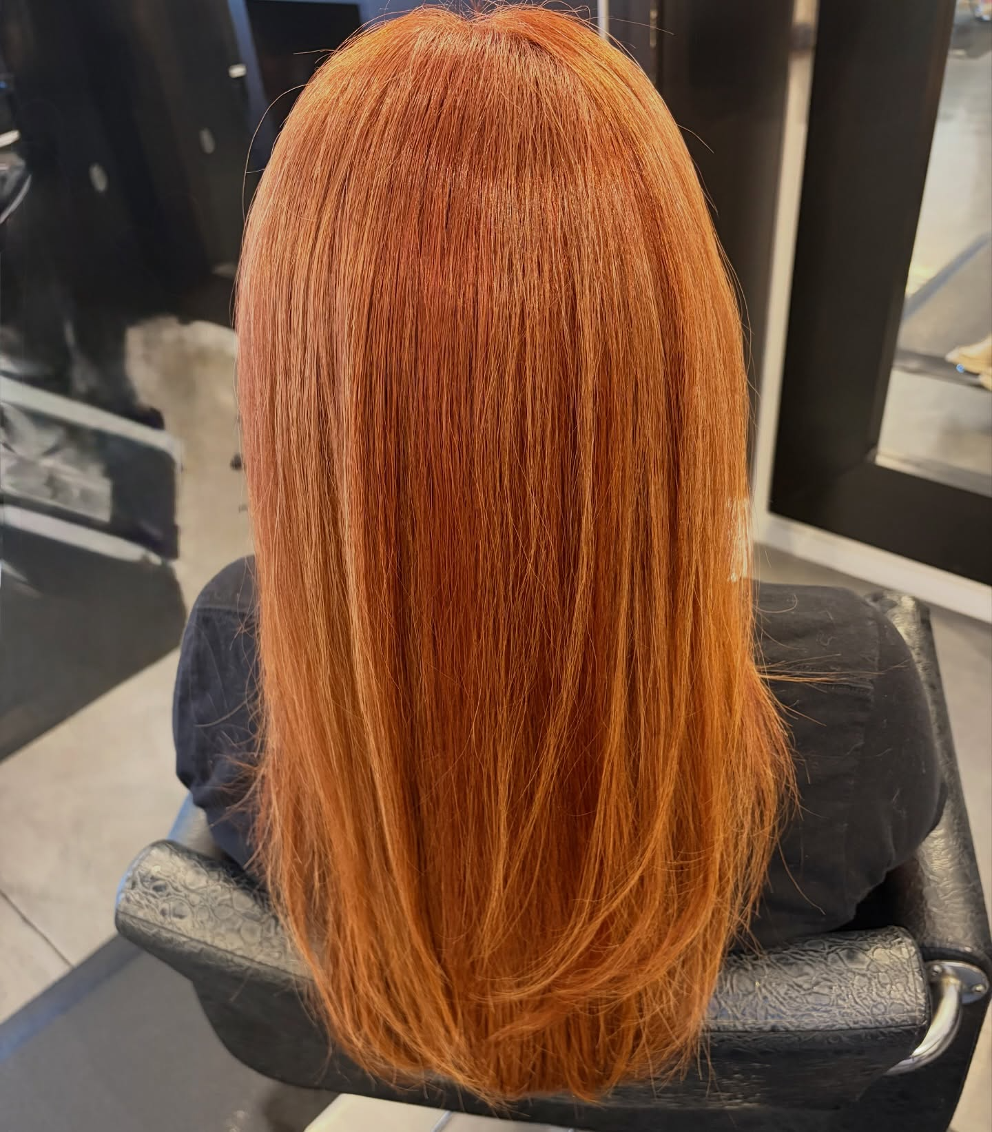 Back view of a person with long, straight, copper-orange hair sitting in a salon chair