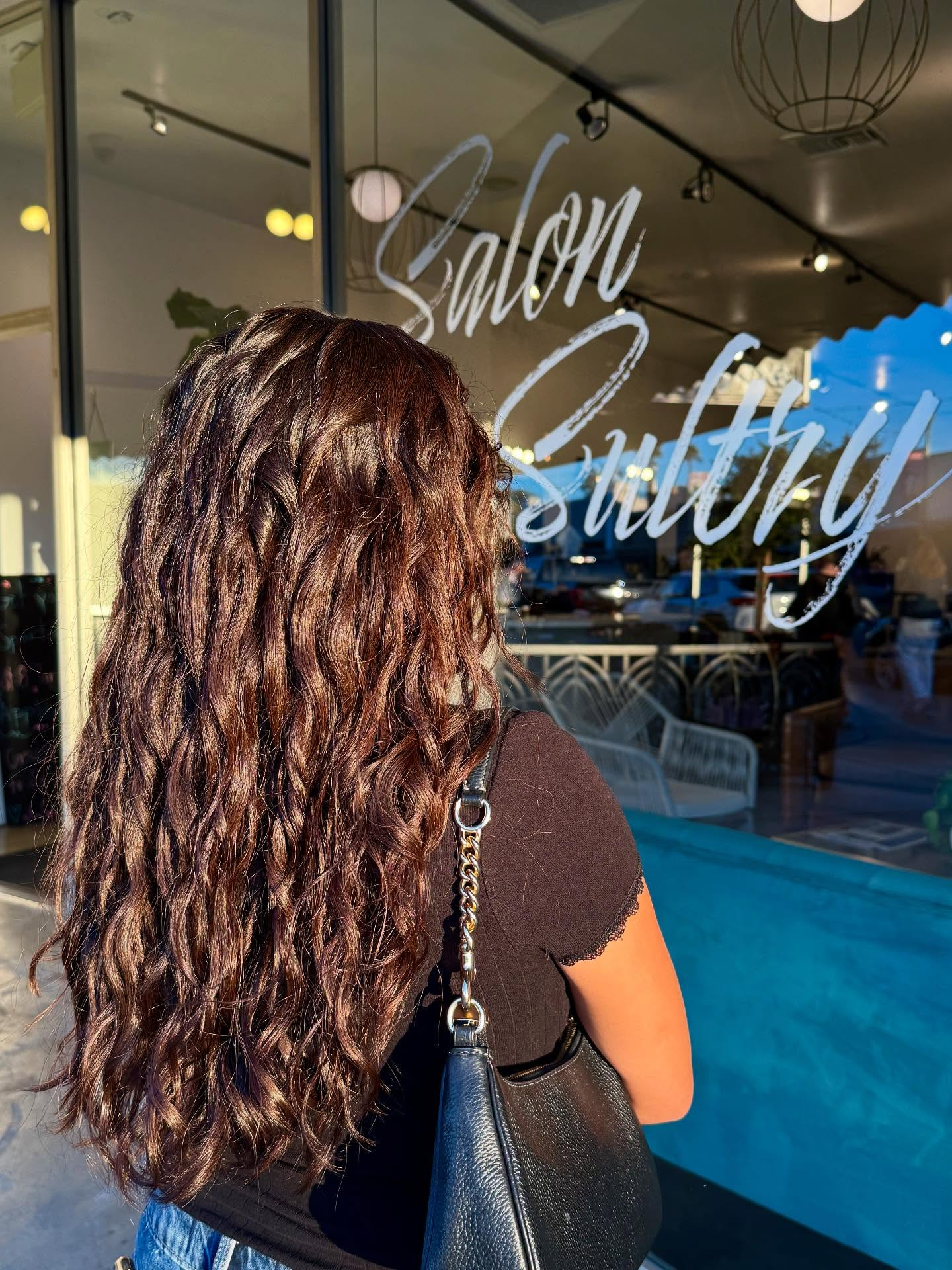 Woman with long wavy hair facing a salon storefront with a neon-style “Salon” sign