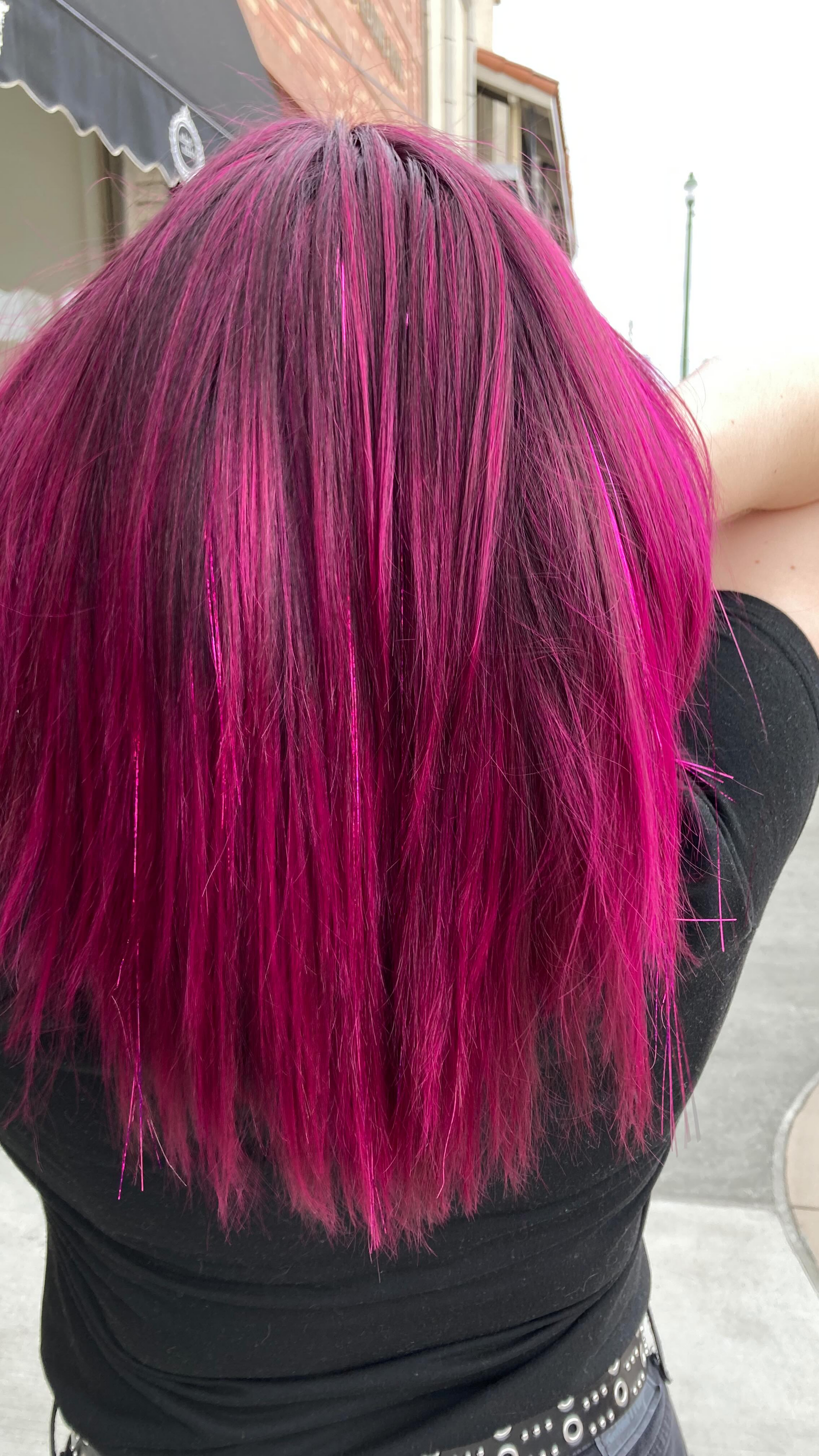 Back view of a person with bright magenta hair wearing a black shirt outdoors