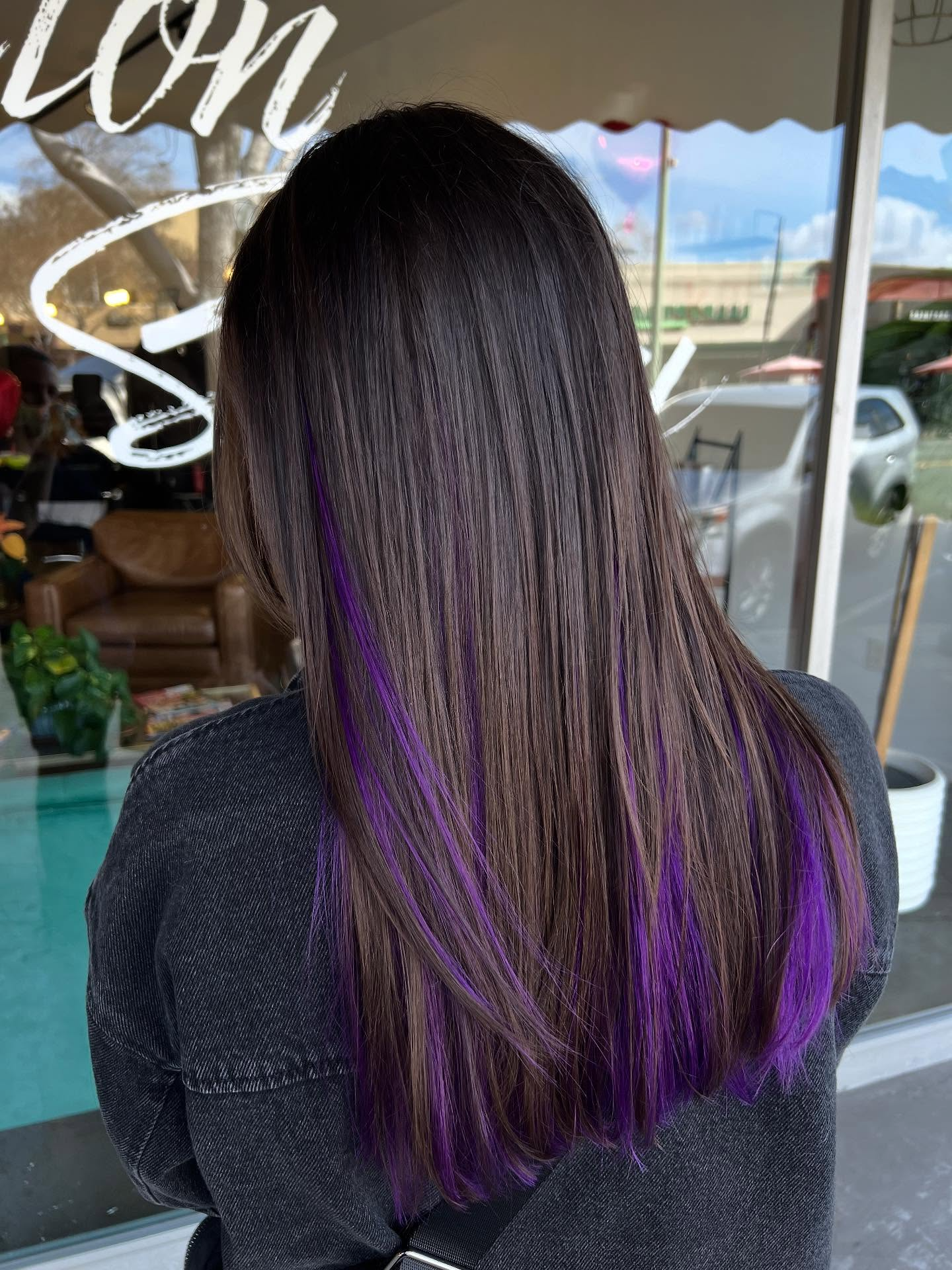 Person with long dark hair and purple highlights seen from behind in a café doorway.