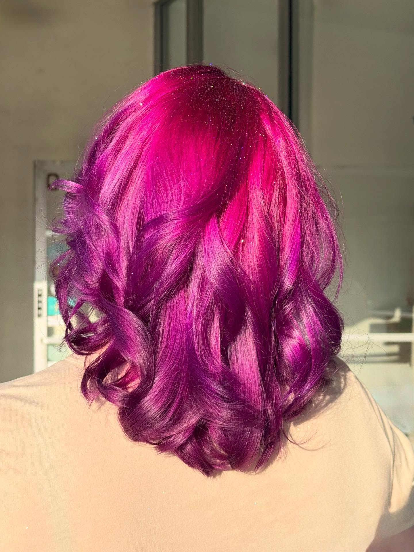 Back view of shoulder-length bright magenta hair with loose curls indoors