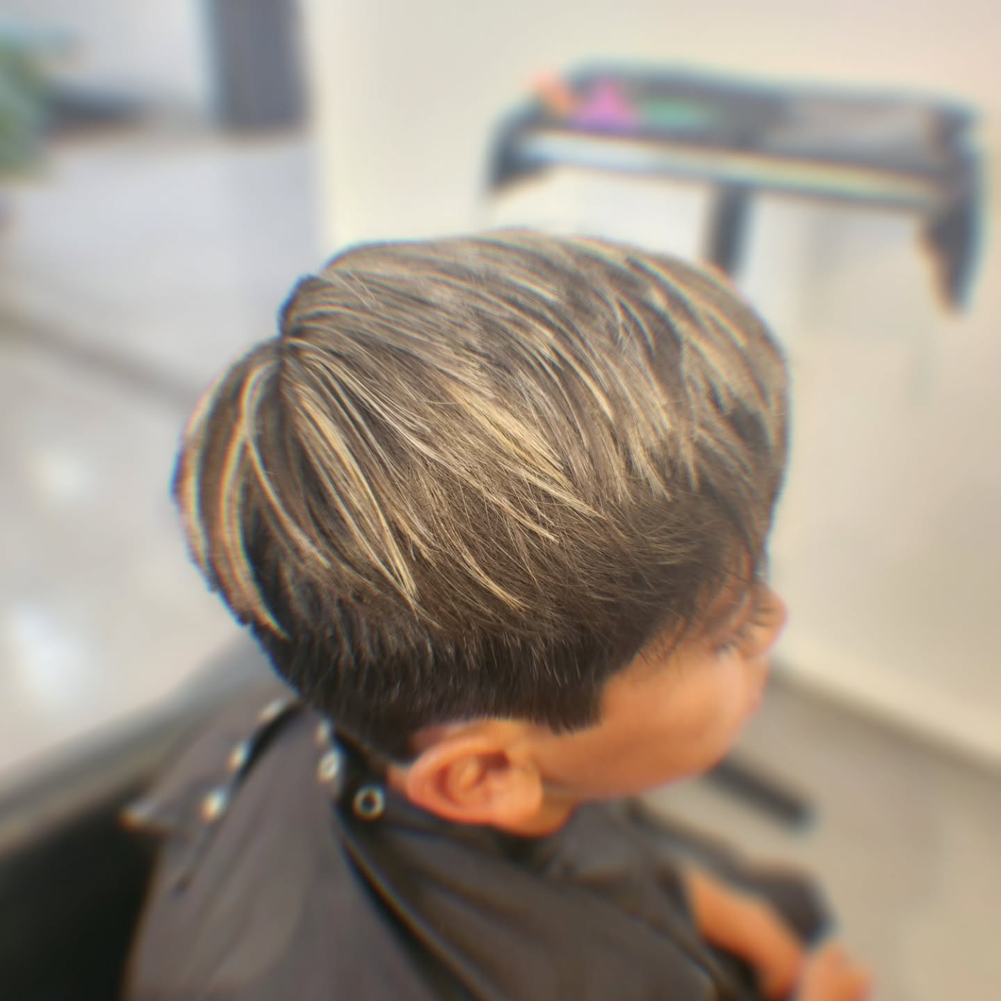 Person with highlighted short hair seated in a salon chair, viewed from above.