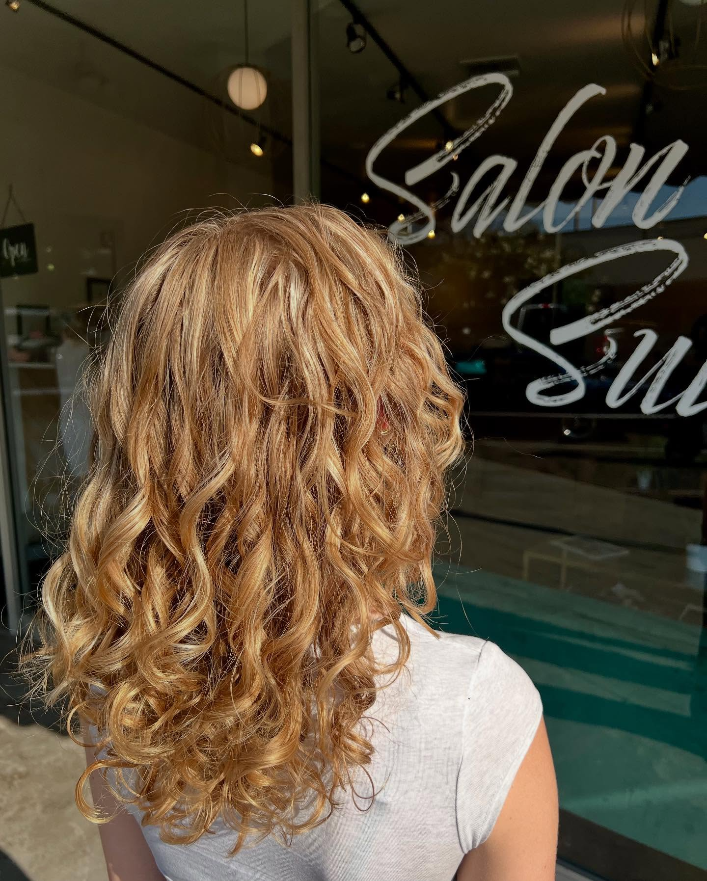 Woman with curly blonde hair seen from behind outside a salon storefront
