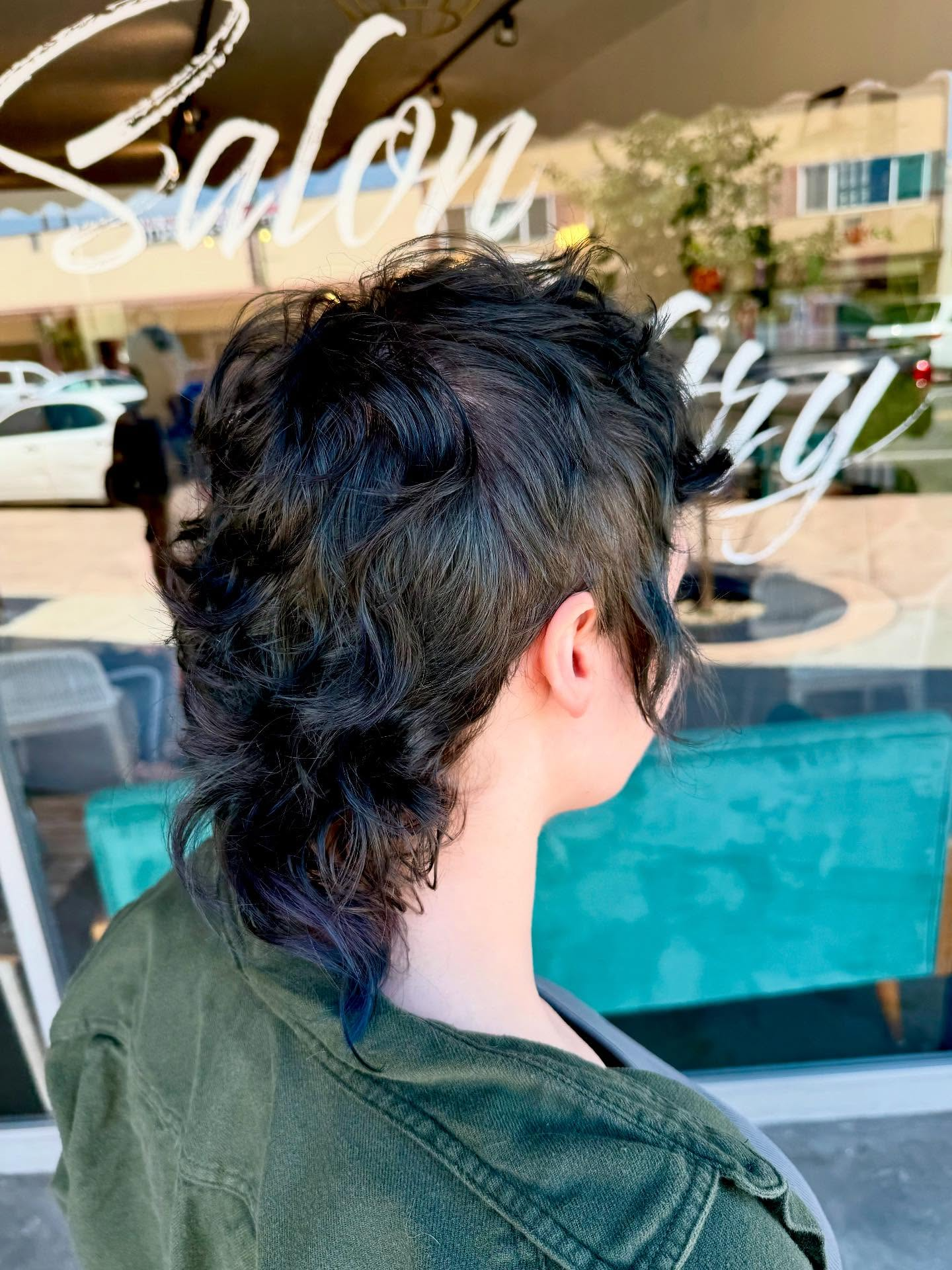 Person with short dark hair seen from behind, sitting by a turquoise pool outside a salon.