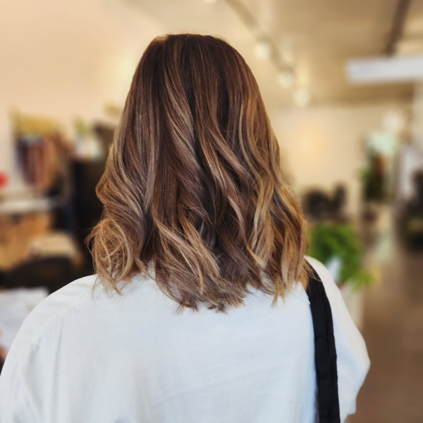 Back view of a person with wavy brown hair in a white top, standing in a softly blurred store interior