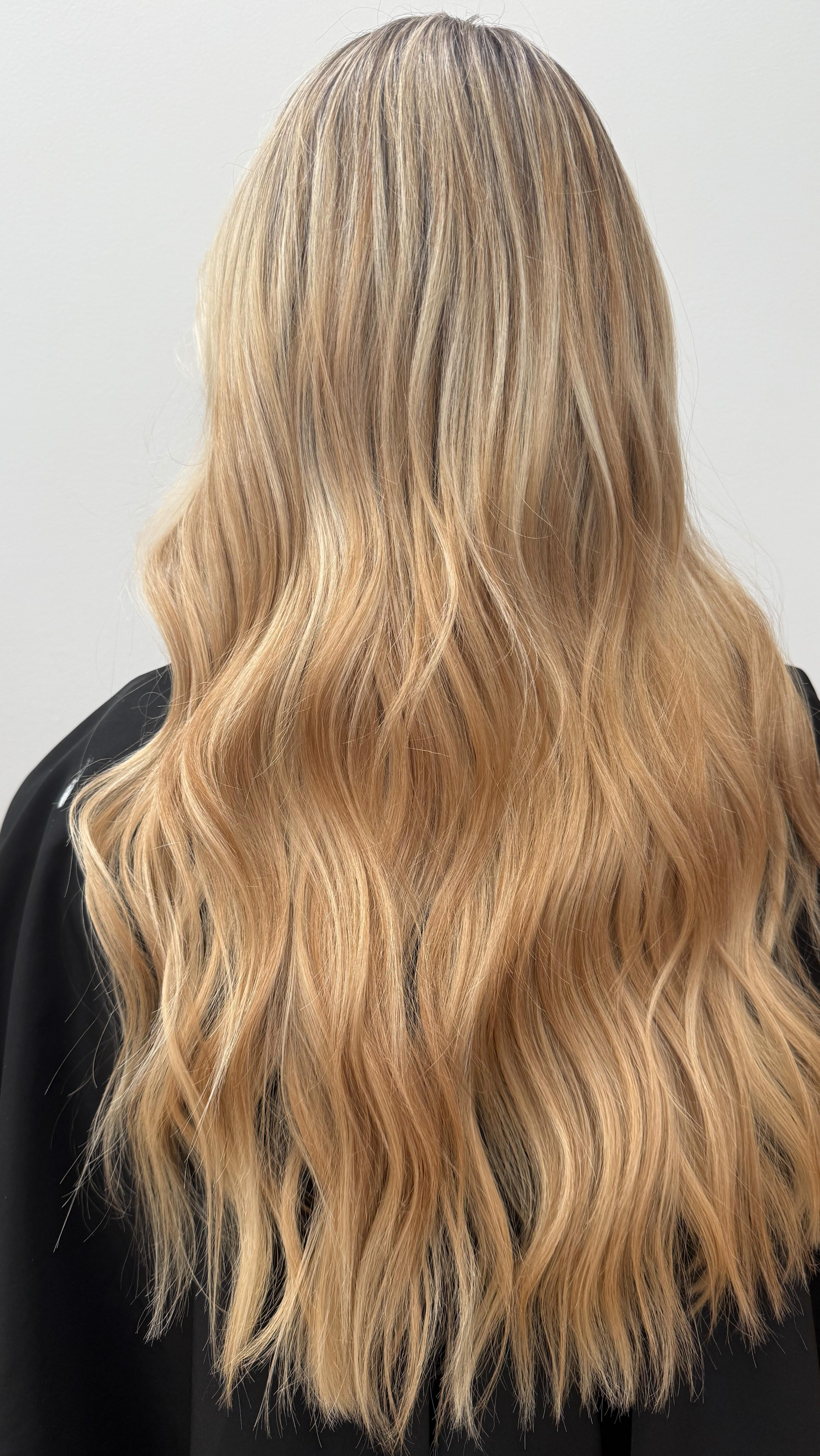 Long wavy blonde hair shown from the back against a plain light background