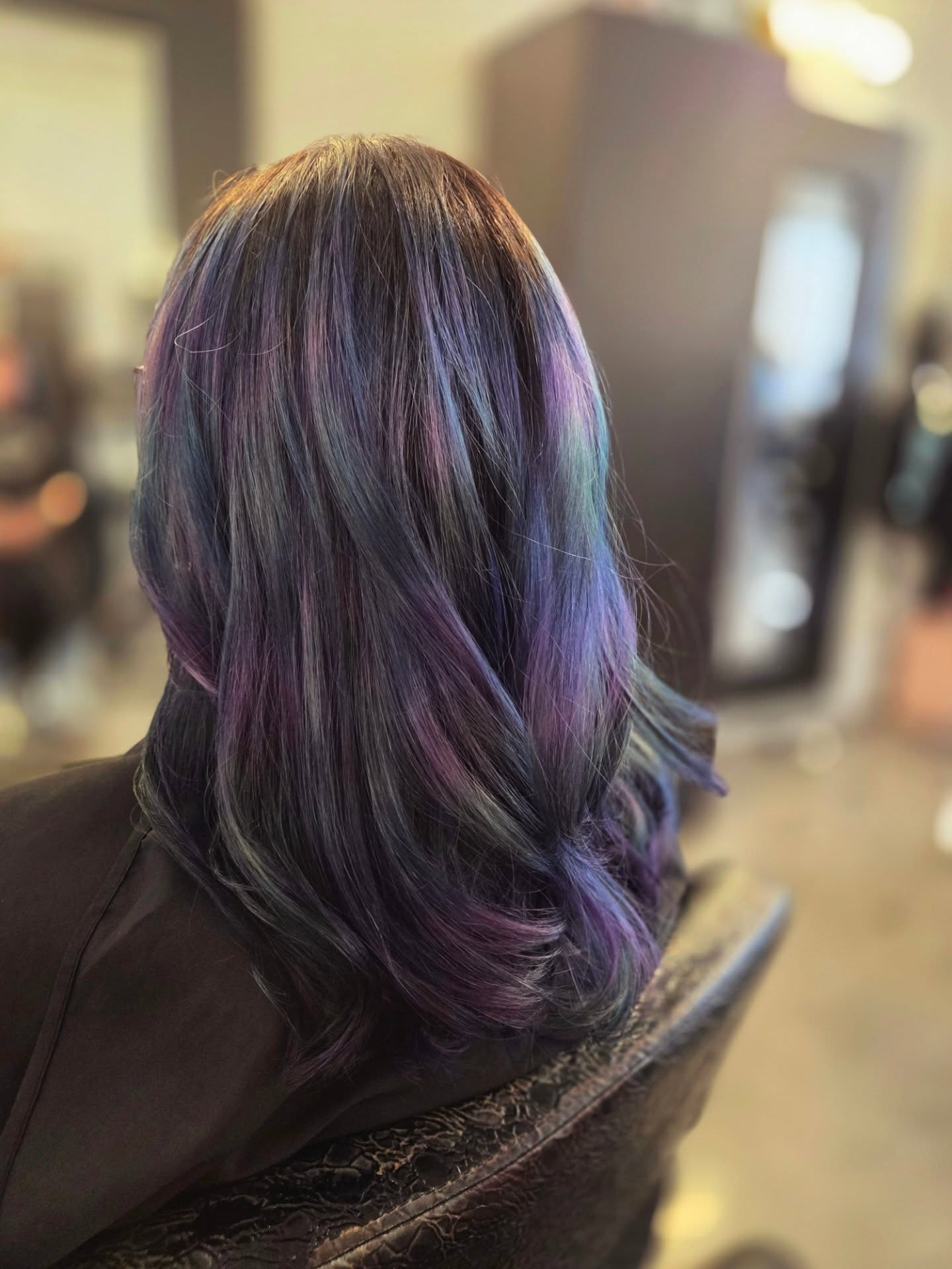 Shiny dark hair with purple highlights in a salon chair, softly blurred salon background