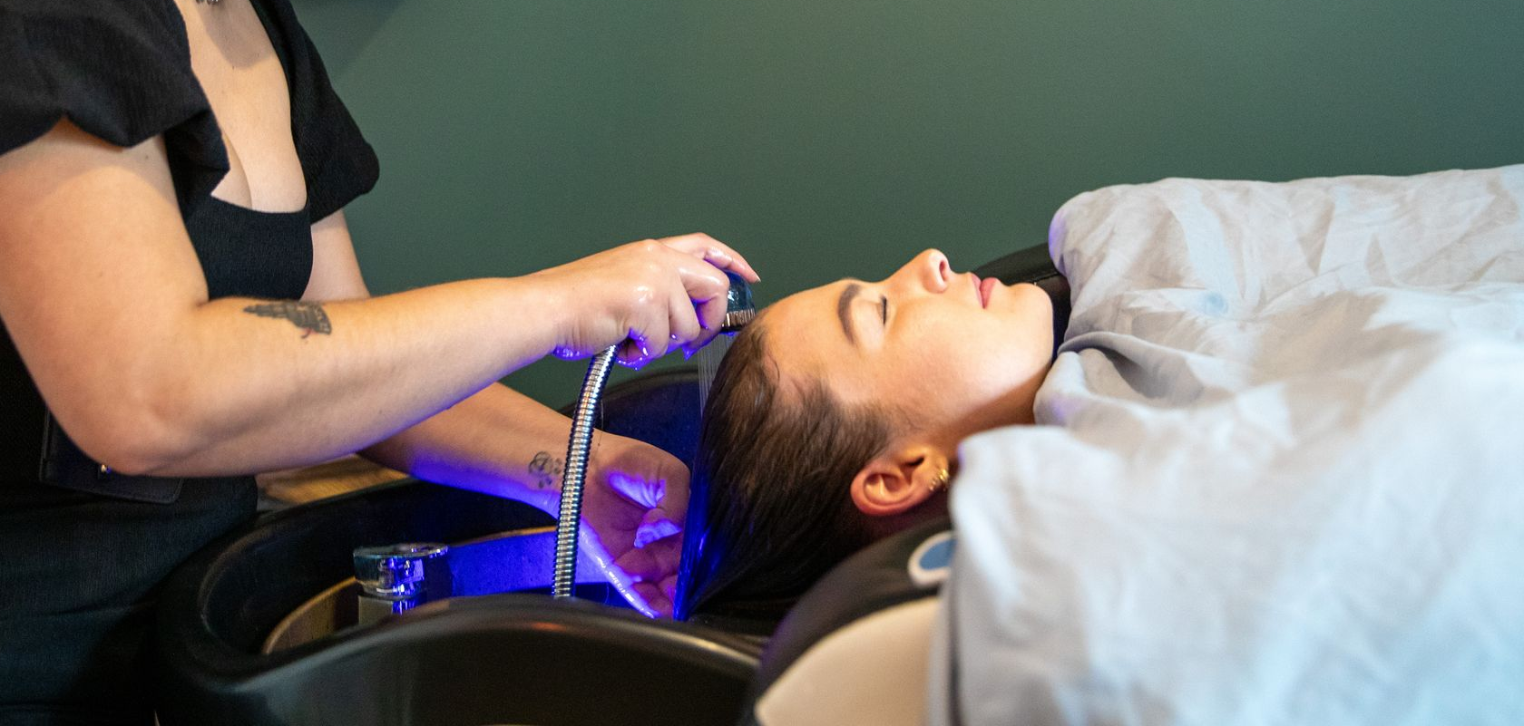 Person undergoing a scalp treatment with purple light in a reclining salon chair