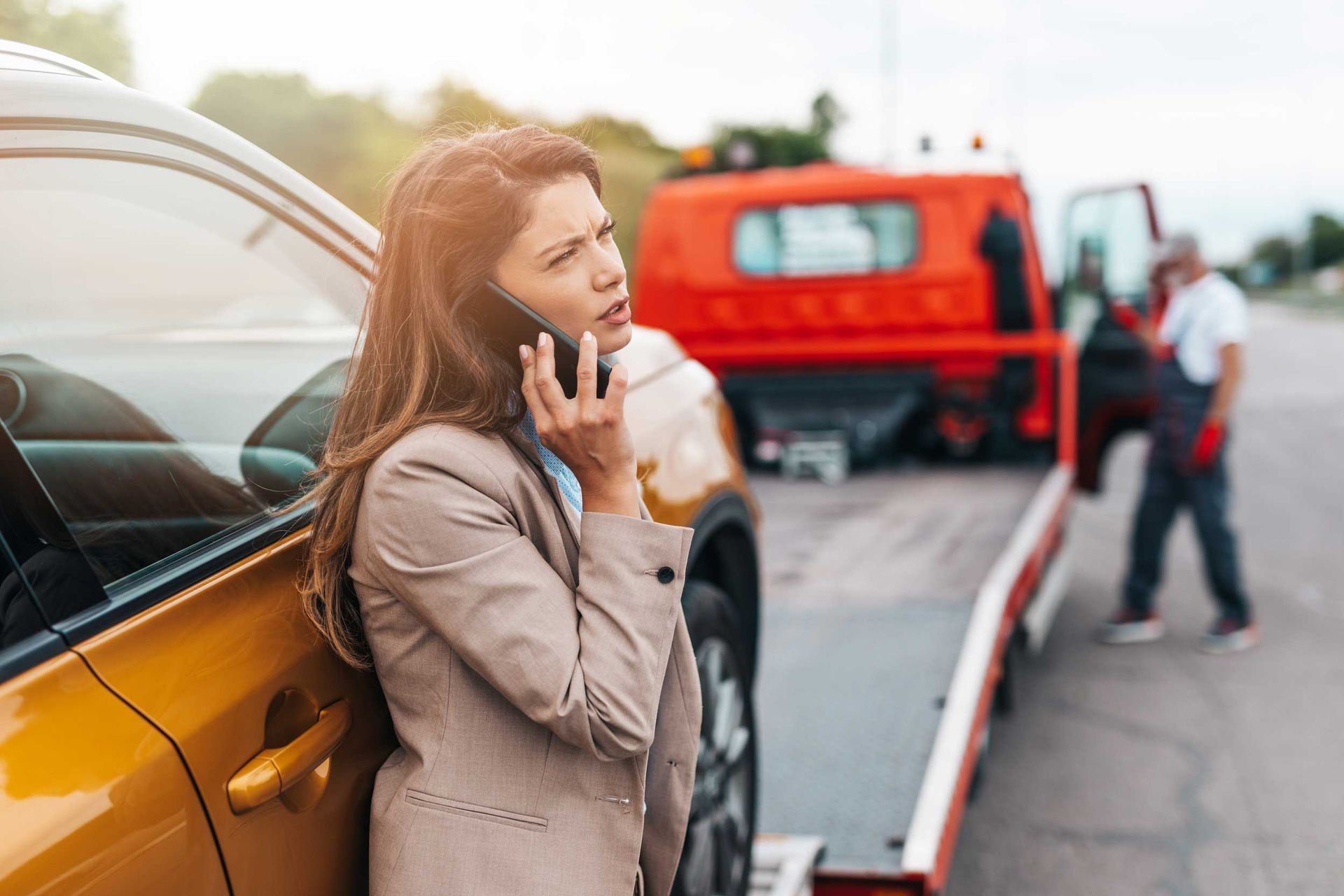 A business woman calling someone while a towing service helps her on the road.
