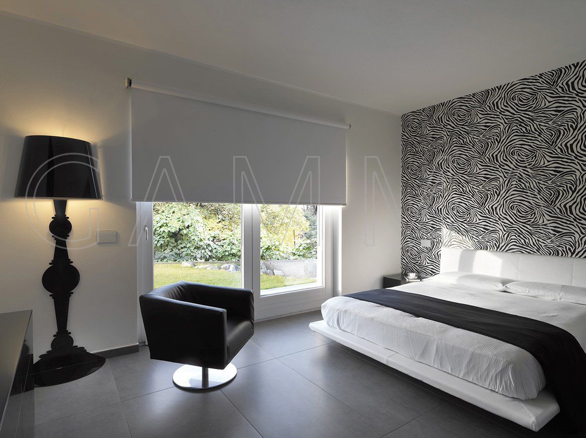 Camera da letto moderna con decorazioni in bianco e nero, ampia finestra e parete decorativa con motivo astratto.